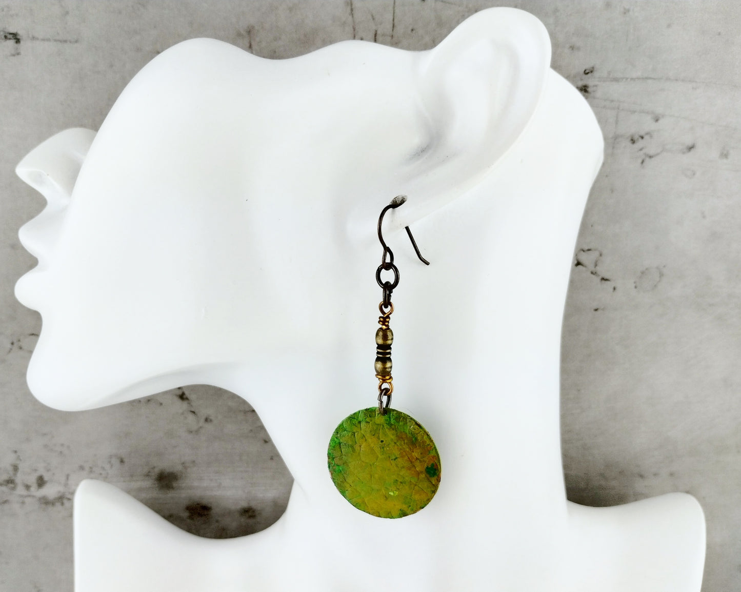 Styled image of dragon skin brass earrings worn, highlighting their mythical design and olive green hues.