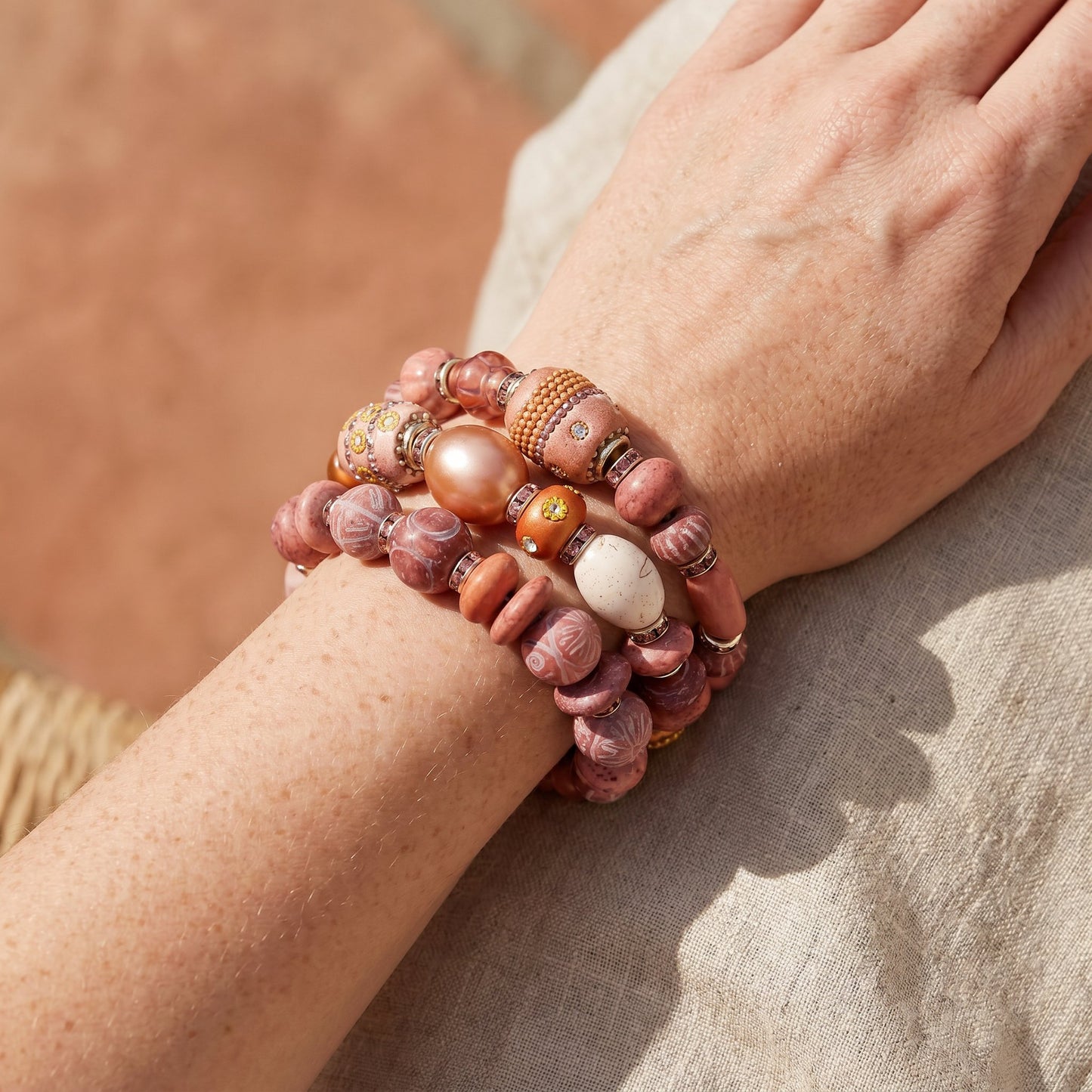 Close-up of a wrist wearing multiple beaded bracelets on a neutral background