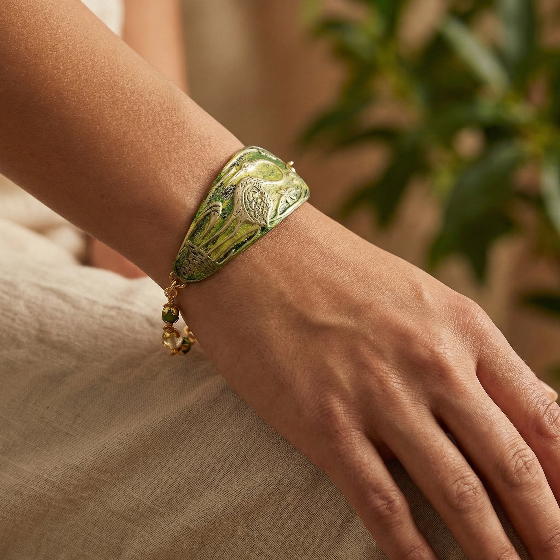 Hand wearing a green bracelet with a bird design on a neutral background