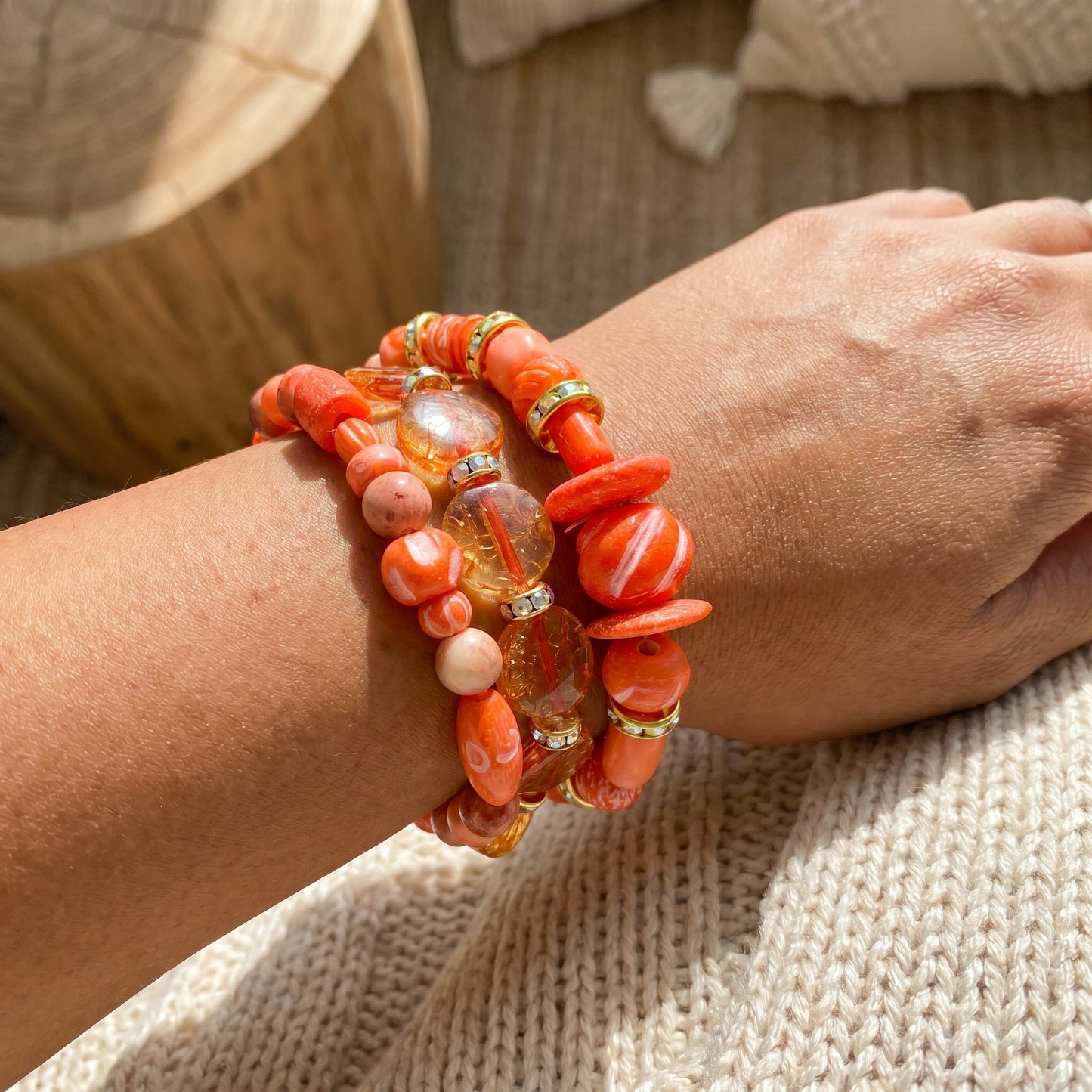 Close-up of a wrist wearing multiple coral-colored beaded bracelets on a textured surface.