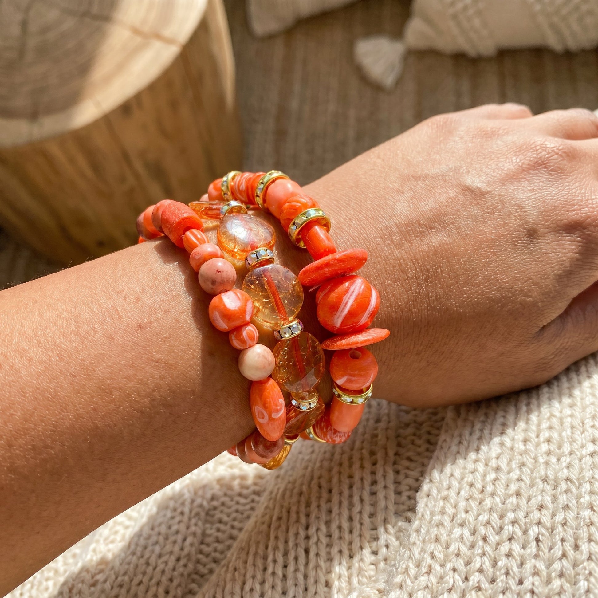 Close-up of a wrist wearing multiple coral-colored beaded bracelets on a textured surface.