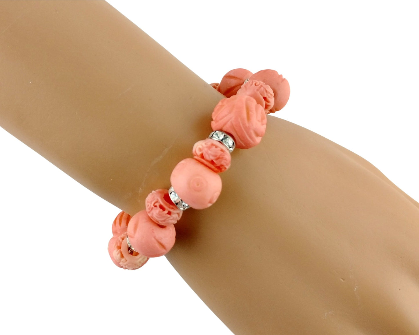 A coral pink beaded bracelet with carved and smooth beads, displayed on a tan mannequin arm against a white background.