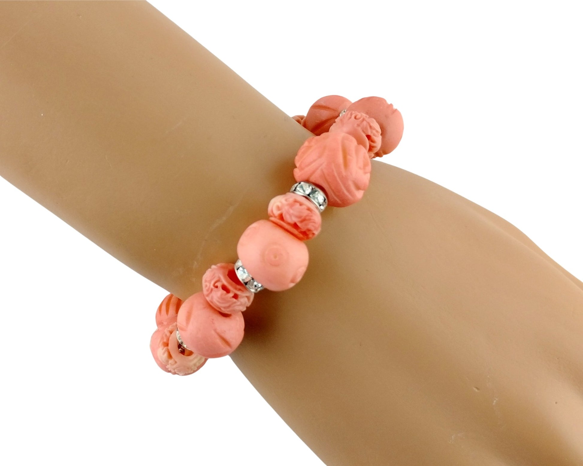 A coral pink beaded bracelet with carved and smooth beads, displayed on a tan mannequin arm against a white background.