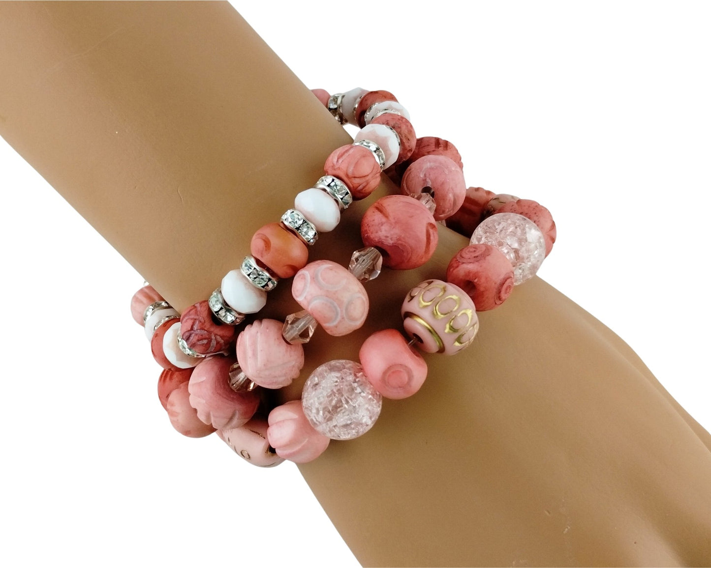 A stack of three beaded bracelets on a tan mannequin wrist. The bracelets feature pink and coral carved beads, white beads with silver metallic accents, and a clear textured bead.
