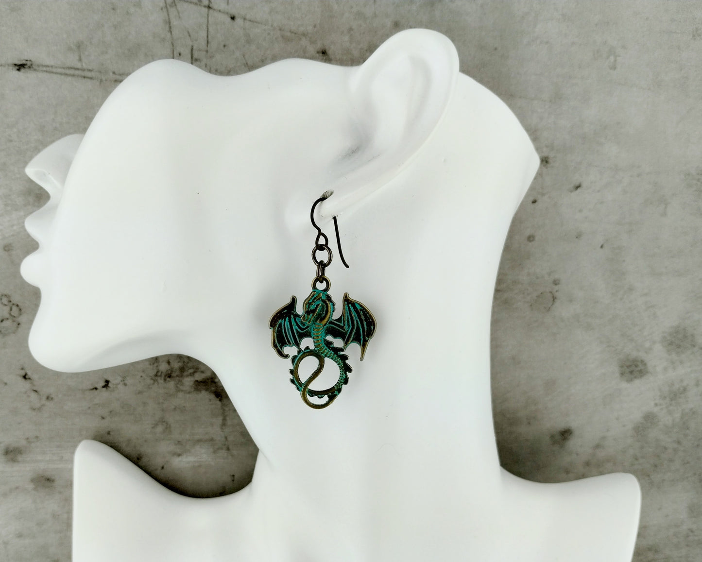 Dragon-shaped earrings on a white mannequin ear against a concrete wall background