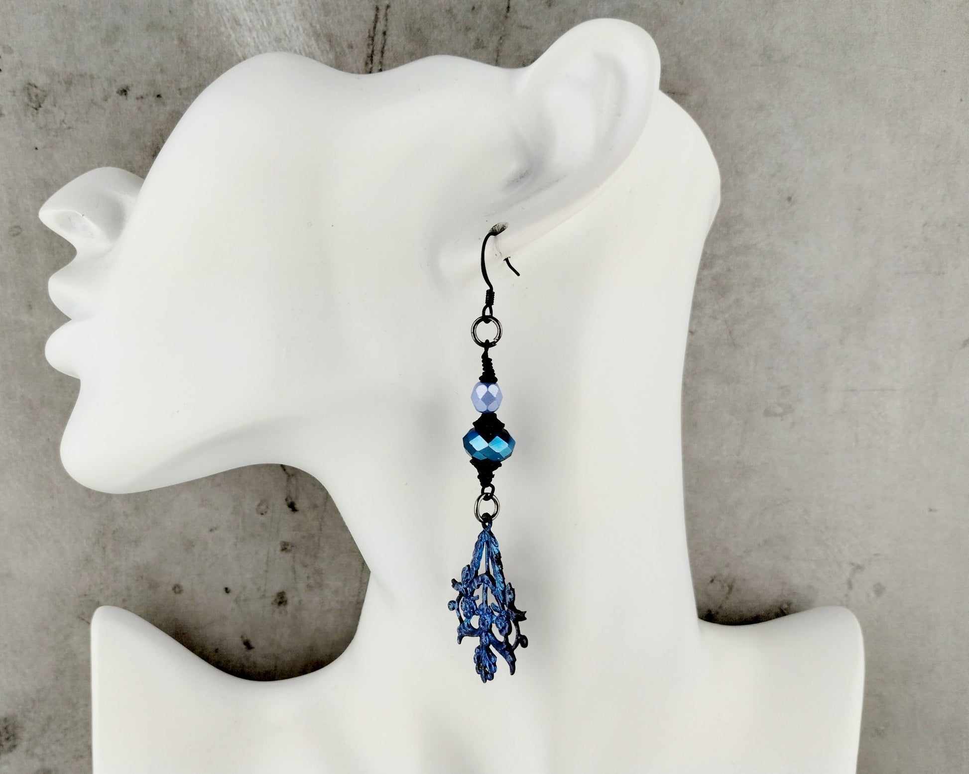 Blue beaded earring on a mannequin ear against a concrete wall background