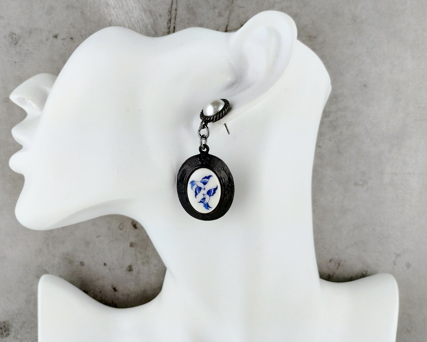 Black oval pendant with blue floral design on a white mannequin bust against a gray background