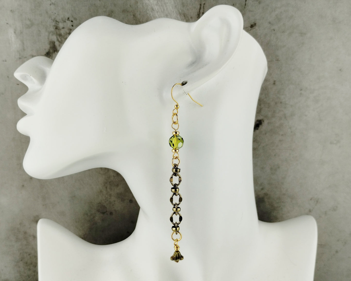 Earring displayed on a white mannequin ear against a concrete wall.