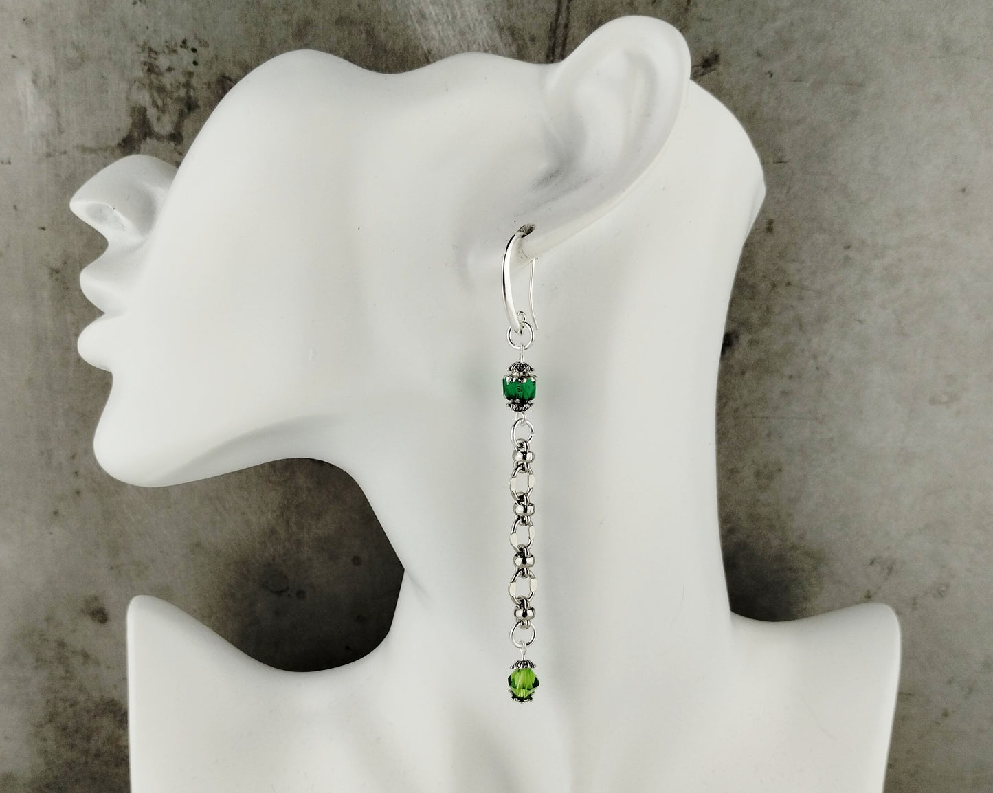 Earring with green gemstones on a white mannequin ear against a gray background