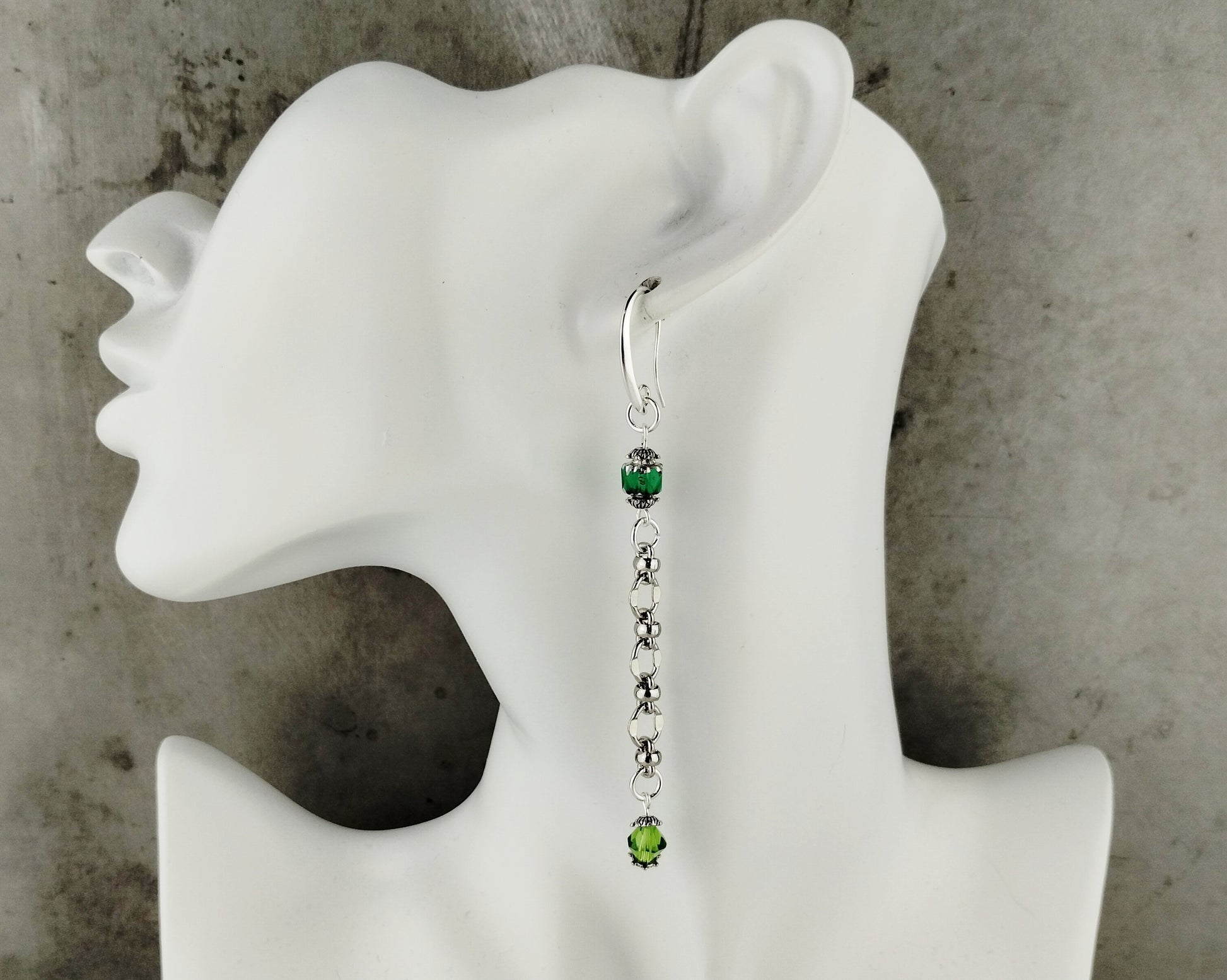 Earring with green gemstones on a white mannequin ear against a gray background