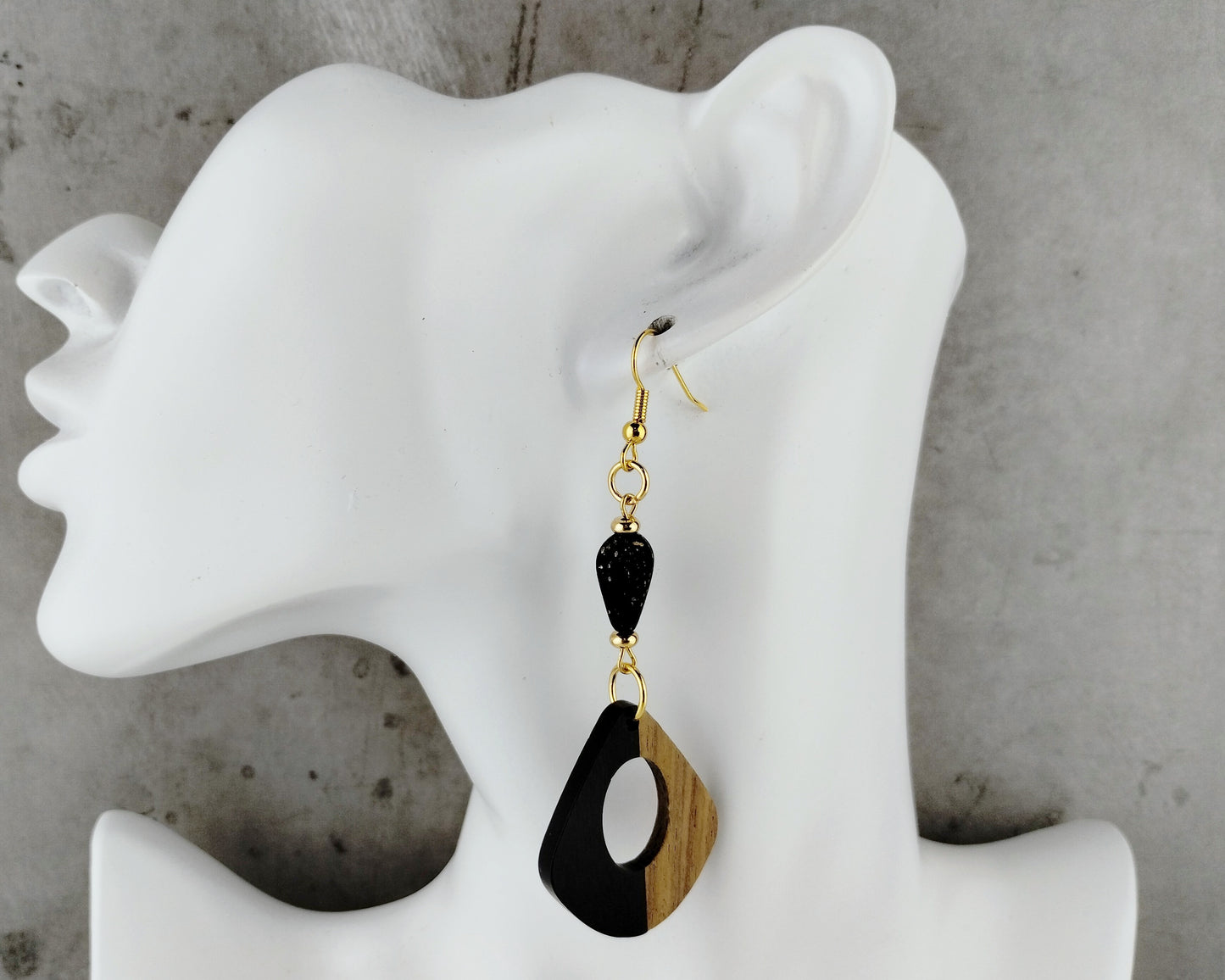 Black and wood earrings on a white mannequin ear against a gray background
