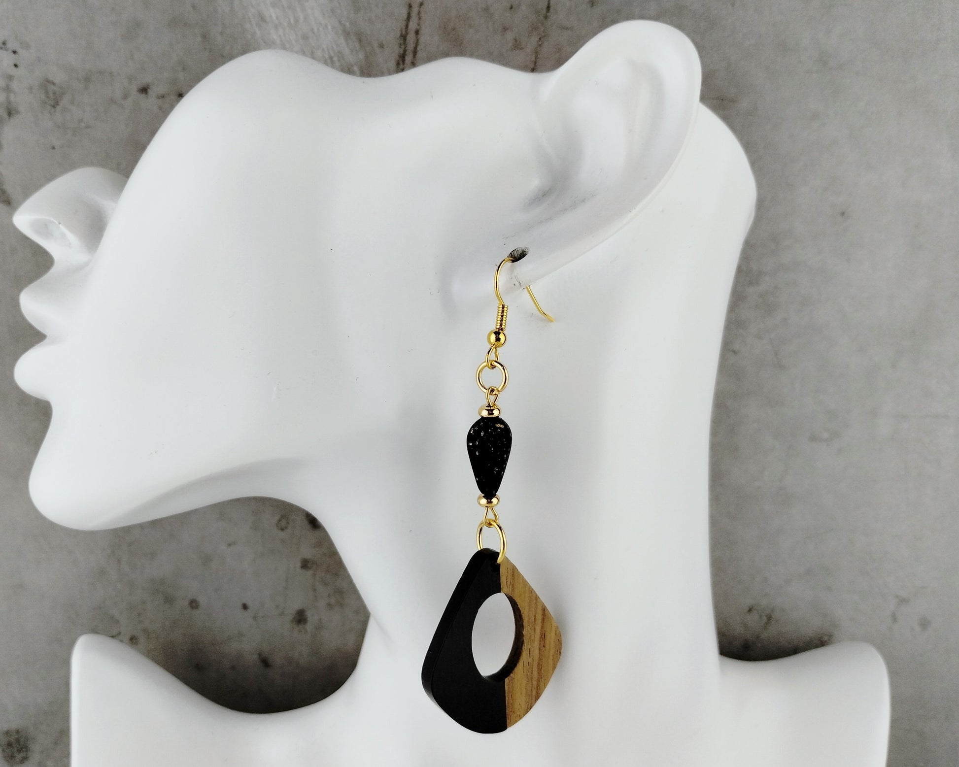 Black and wood earrings on a white mannequin ear against a gray background
