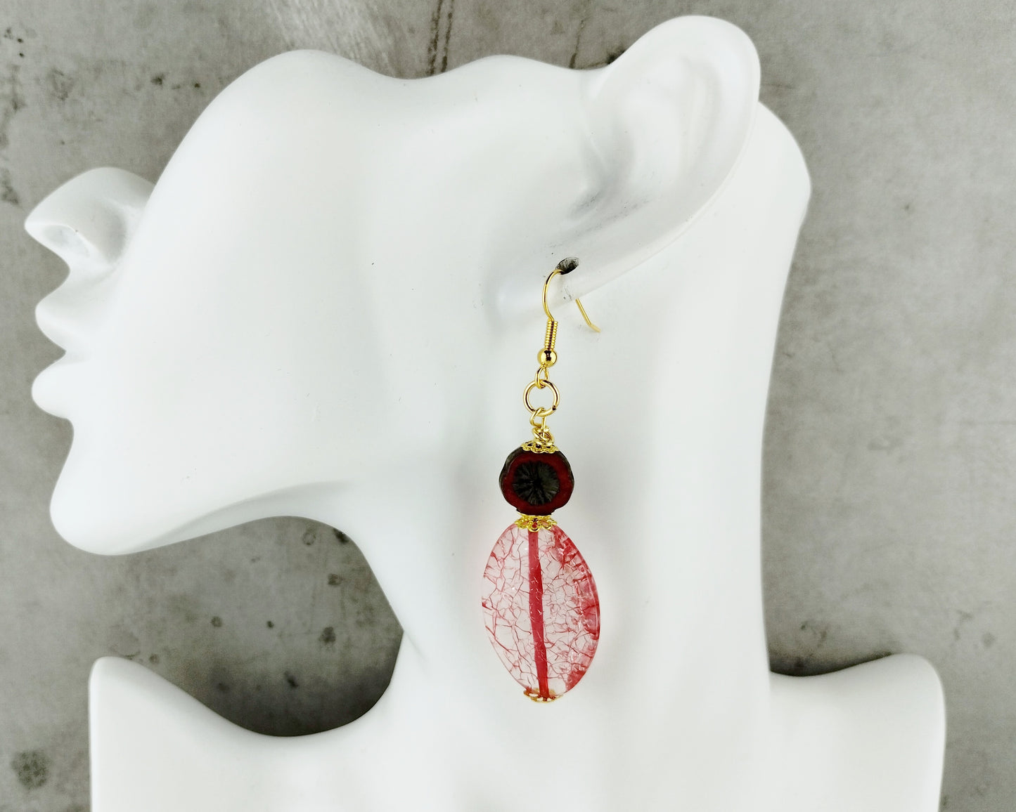 Earrings with red and gold design on a white mannequin ear