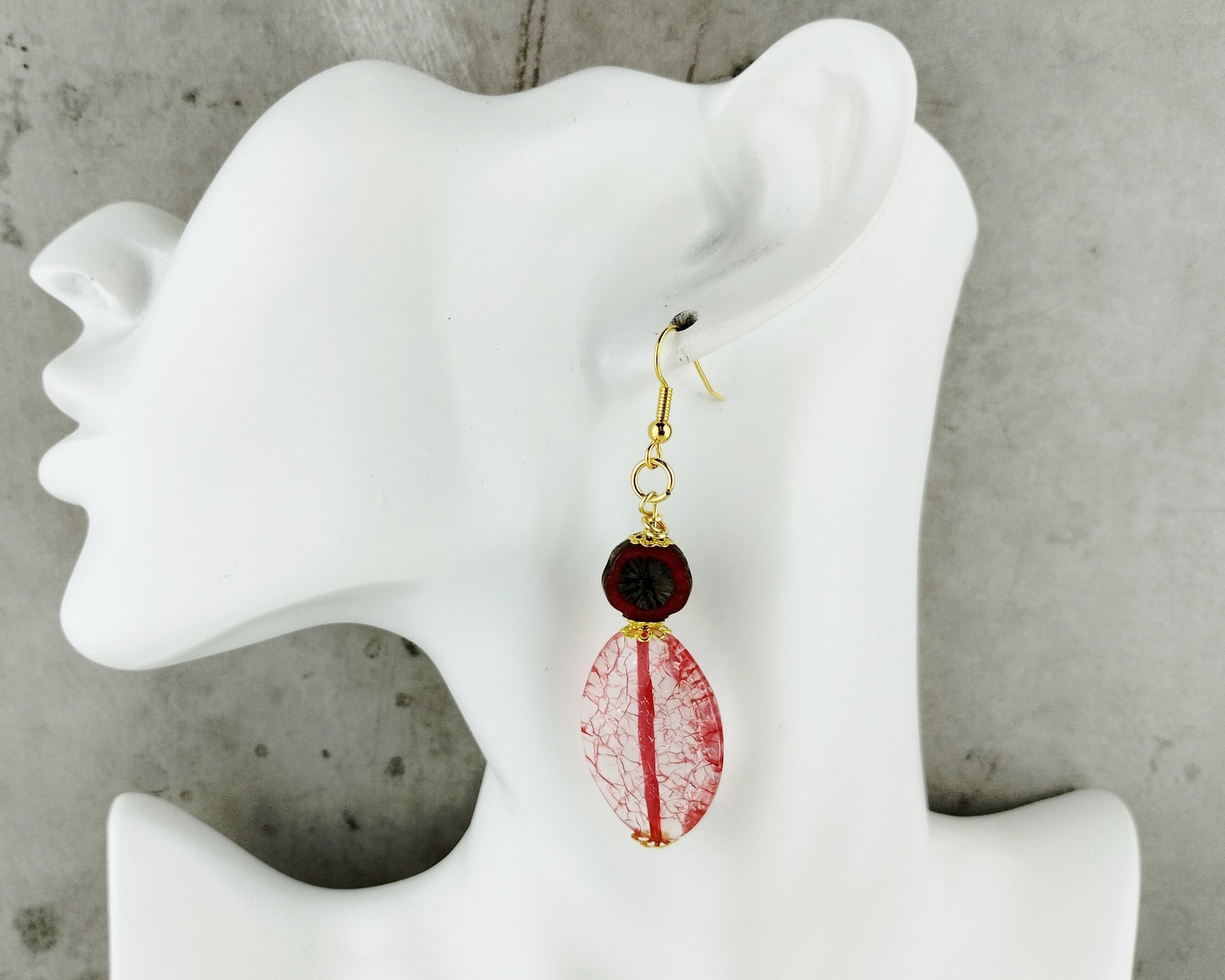 Earrings with red and gold design on a white mannequin ear