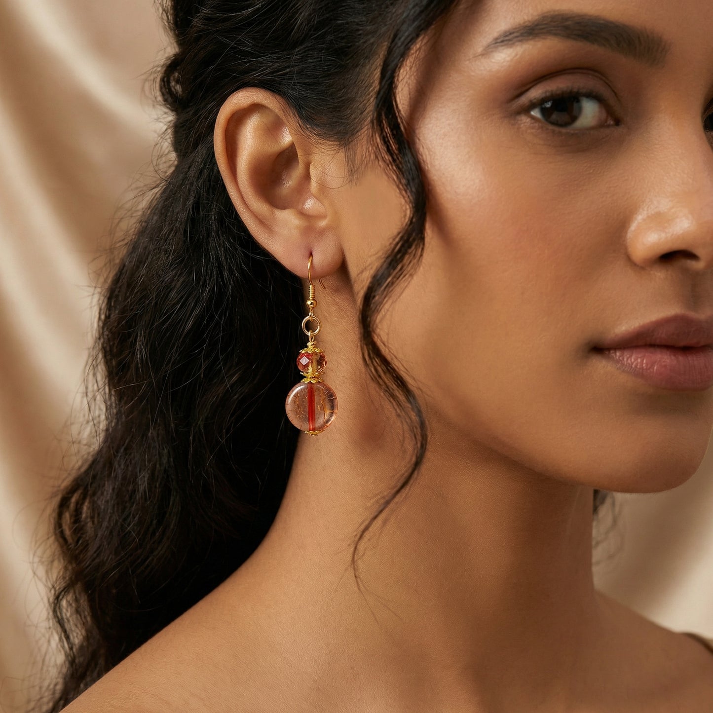 Close-up of a woman wearing gold earrings with red beads against a beige background