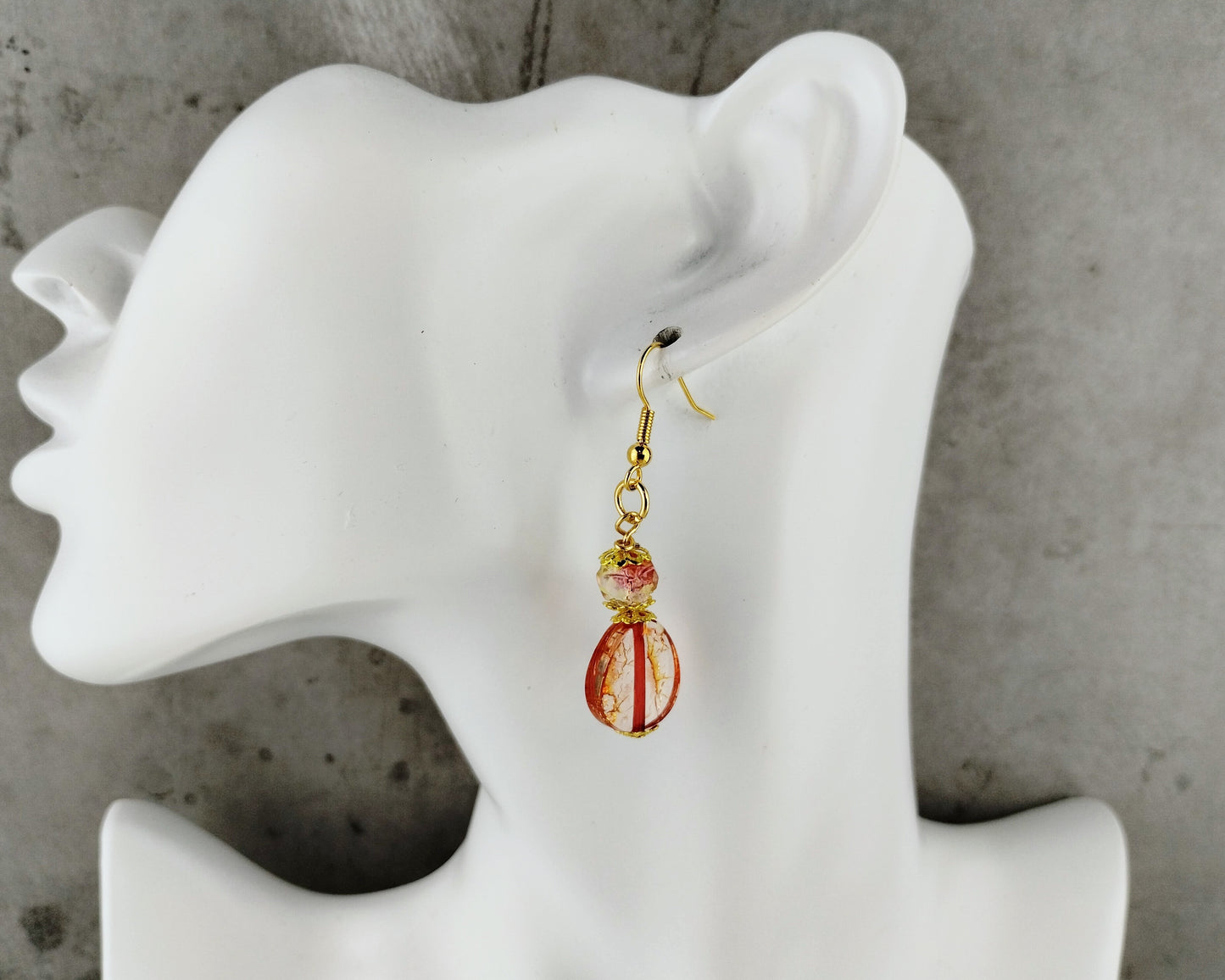 Earring displayed on a mannequin ear with a concrete background