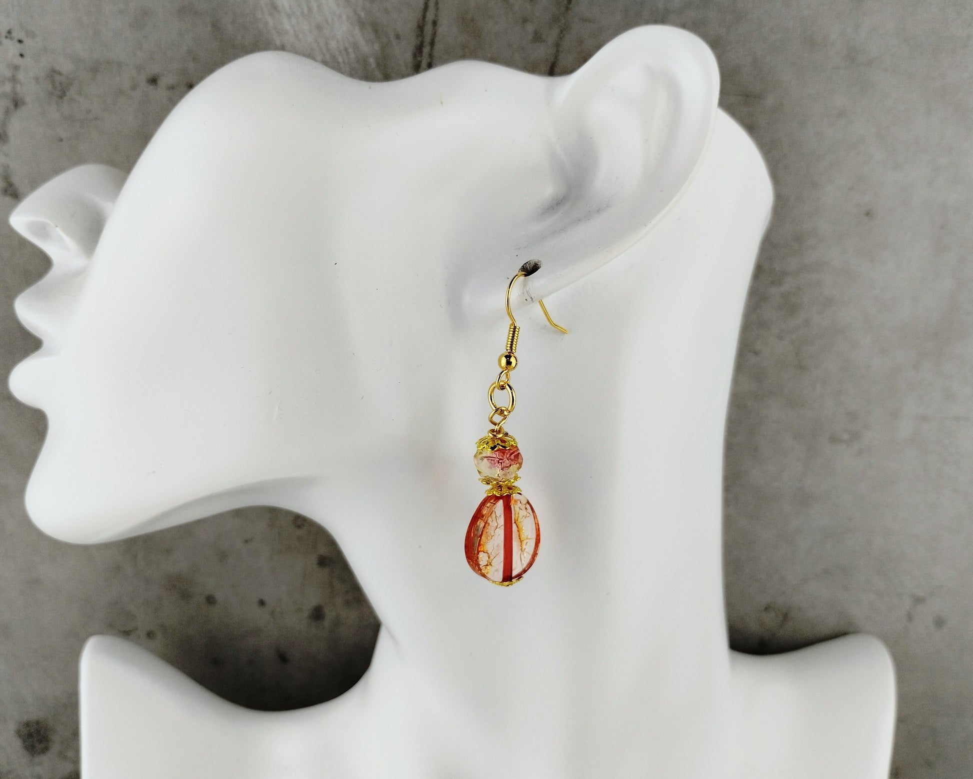 Earring displayed on a mannequin ear with a concrete background