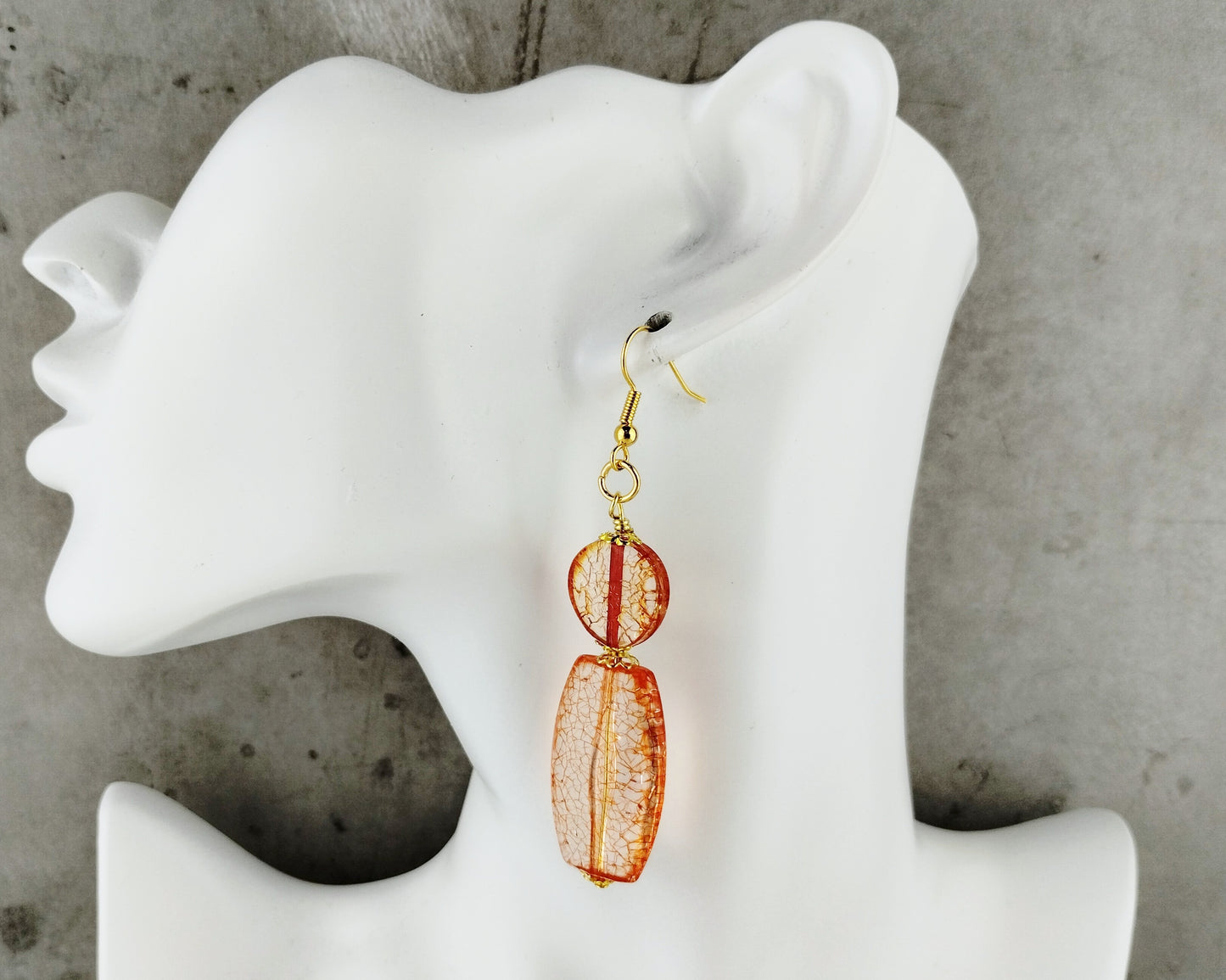 Orange earrings on a white mannequin ear against a gray concrete background