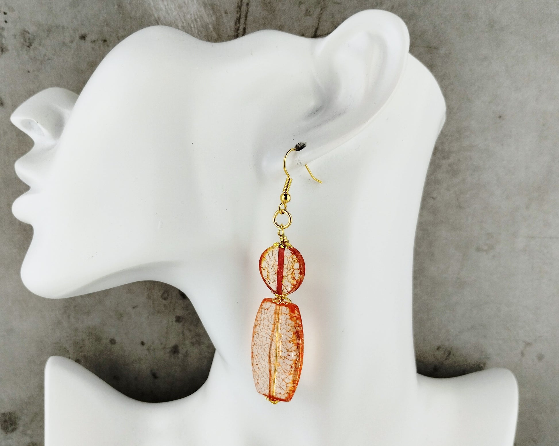 Orange earrings on a white mannequin ear against a gray concrete background
