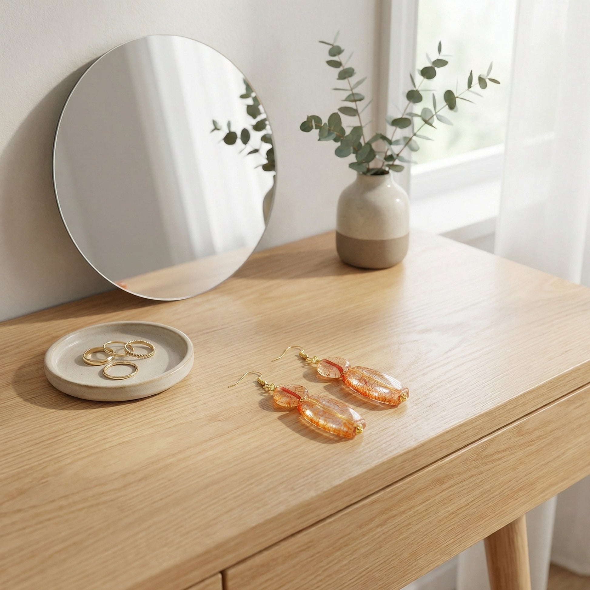 Orange earrings on a wooden surface with a mirror and plant in the background