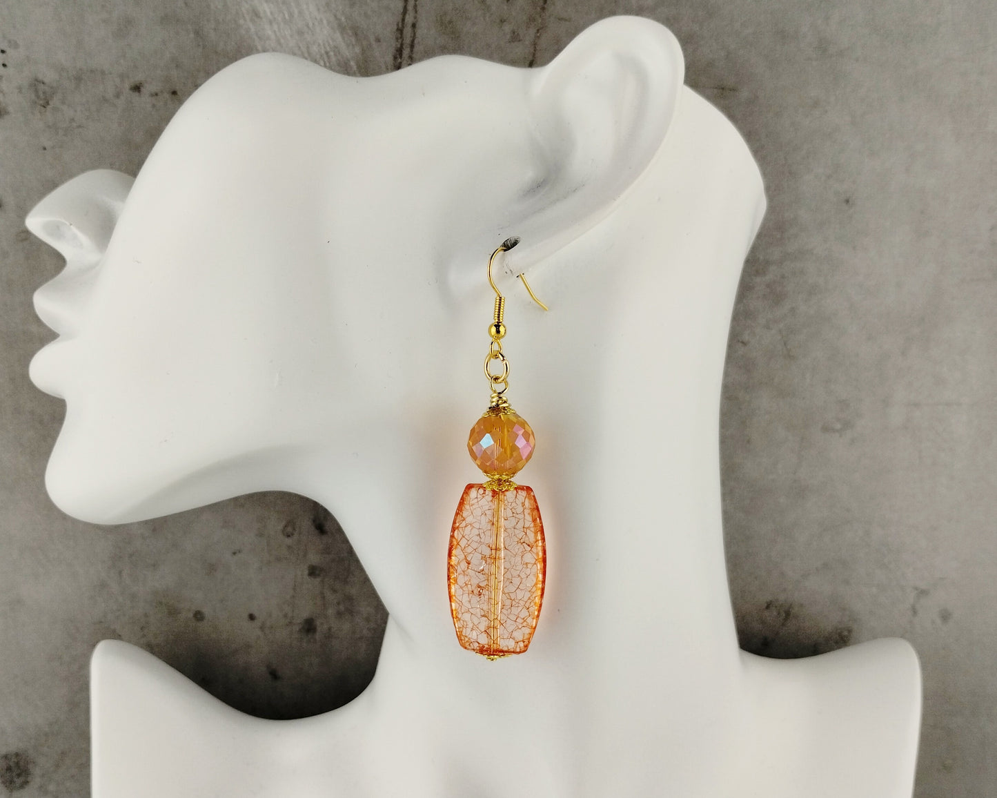 Orange beaded earrings on a white mannequin ear against a gray background