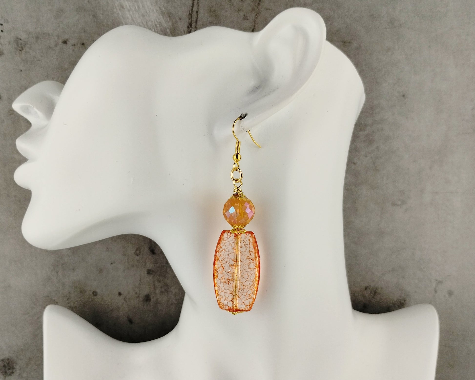 Orange beaded earrings on a white mannequin ear against a gray background