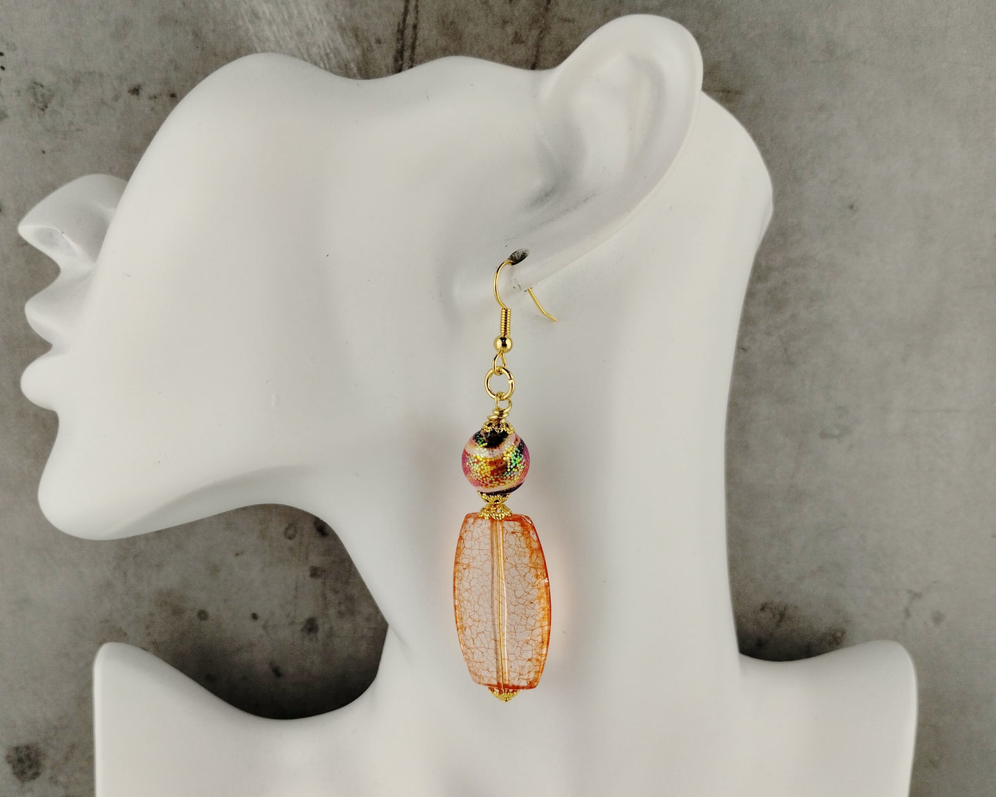 Gold and orange beaded earring on a white mannequin ear against a gray background