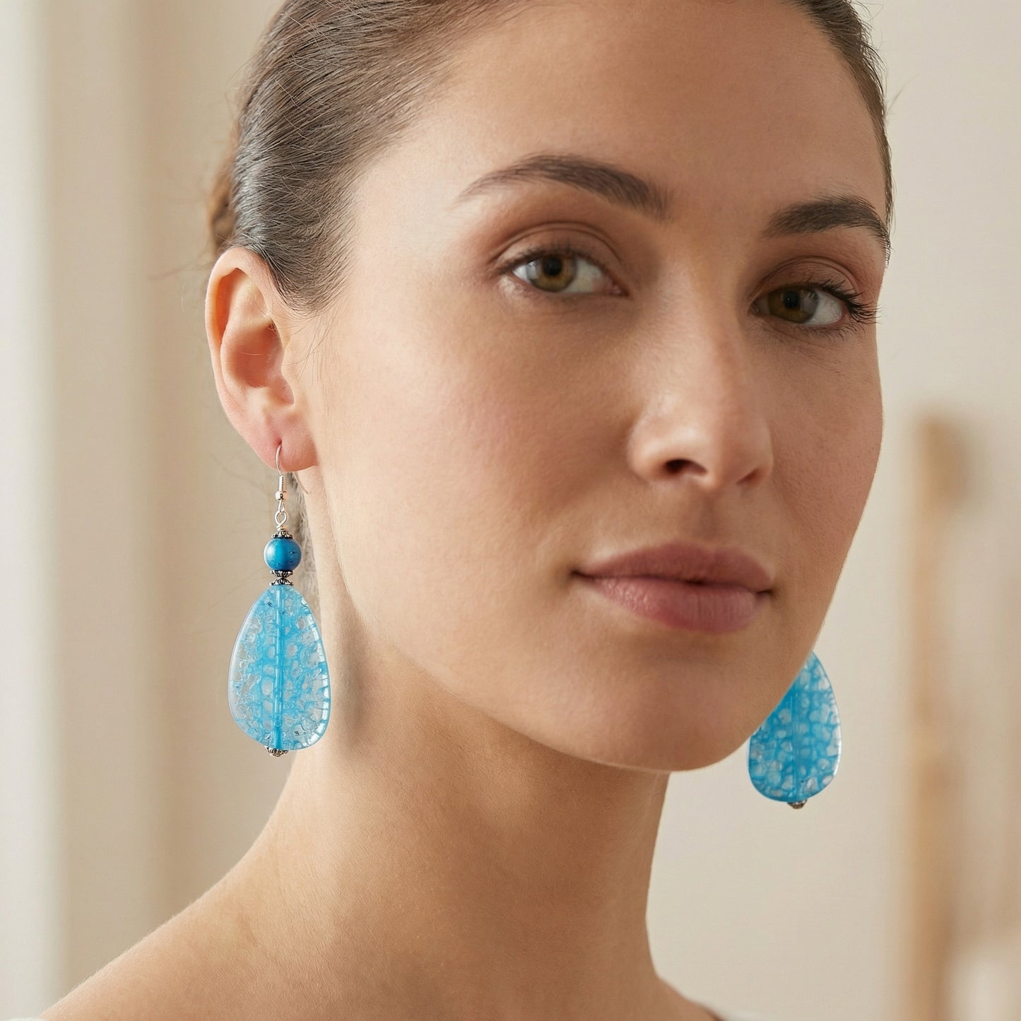 Woman wearing blue teardrop earrings with a neutral background