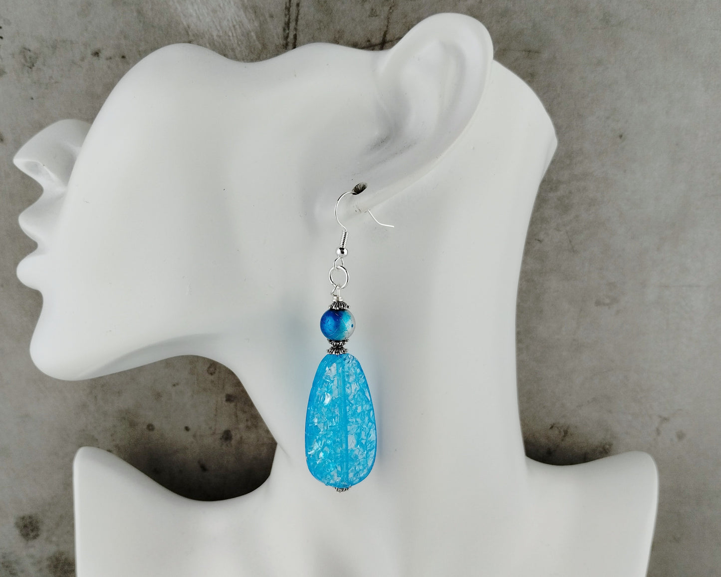 Blue teardrop earrings on a white mannequin ear against a gray background