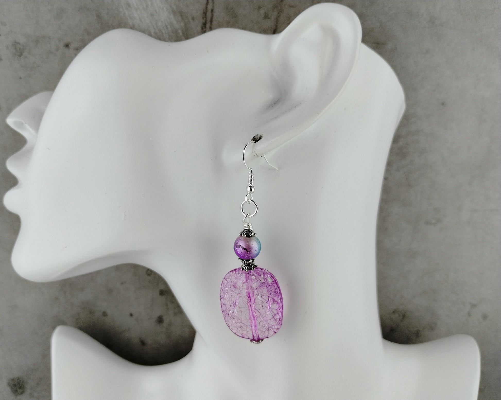 Purple beaded earring on a white mannequin ear against a gray background