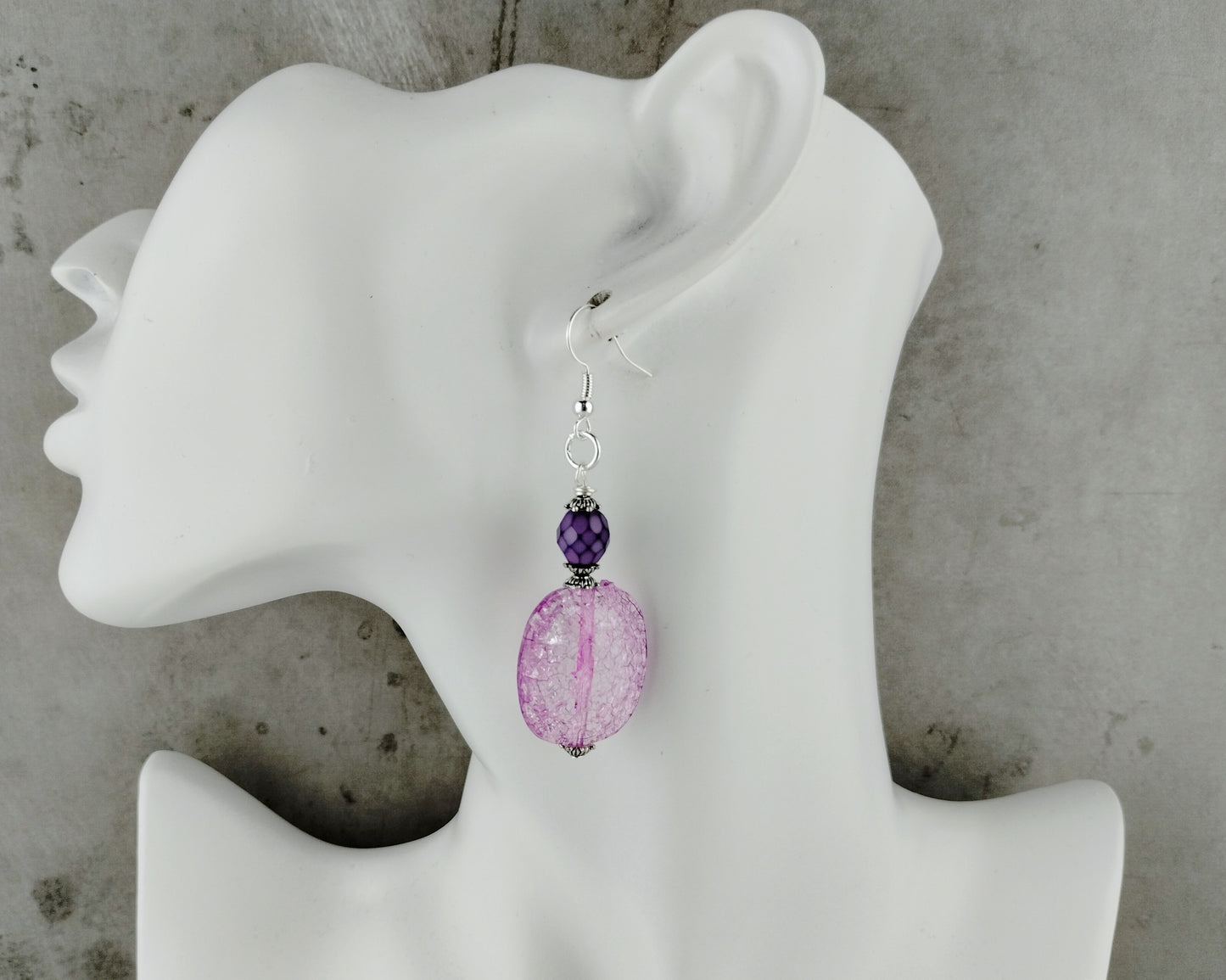 Purple beaded earrings on a white mannequin ear against a gray background