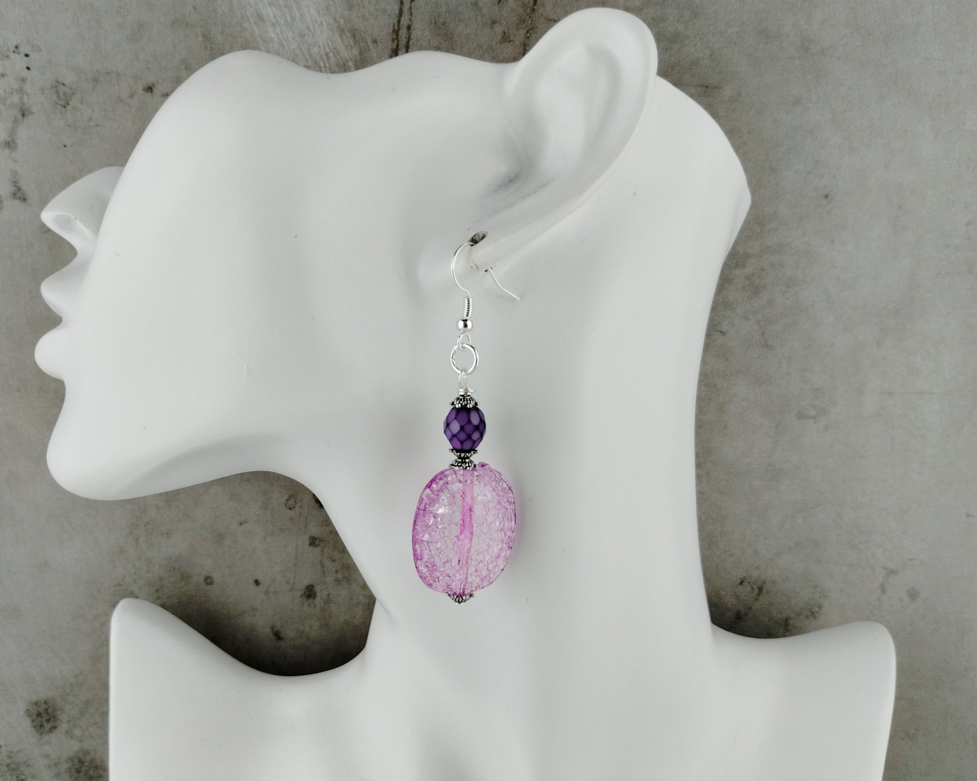 Purple beaded earrings on a white mannequin ear against a gray background
