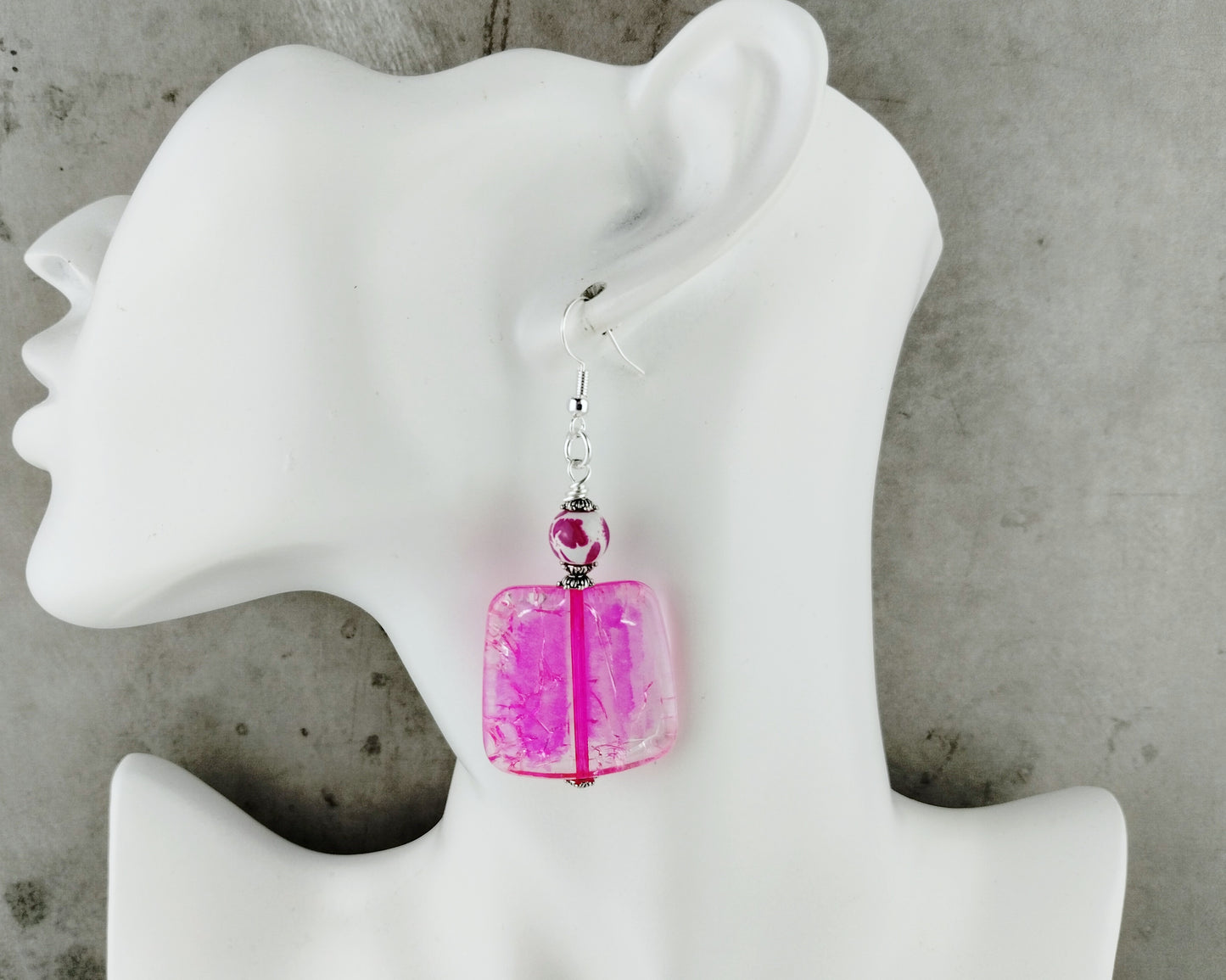 Pink earrings on a white mannequin ear with a gray background