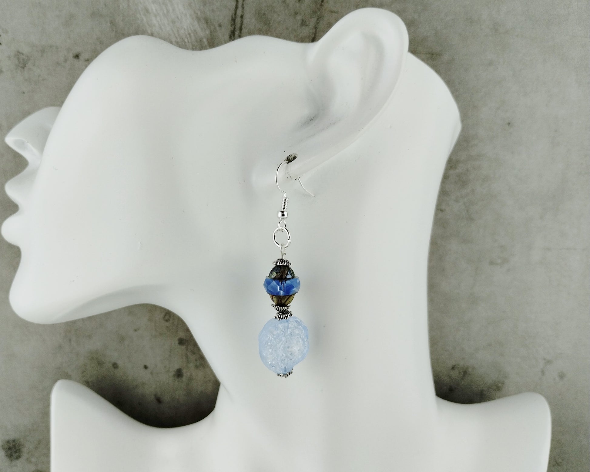 Blue beaded earring on a white mannequin ear against a gray background