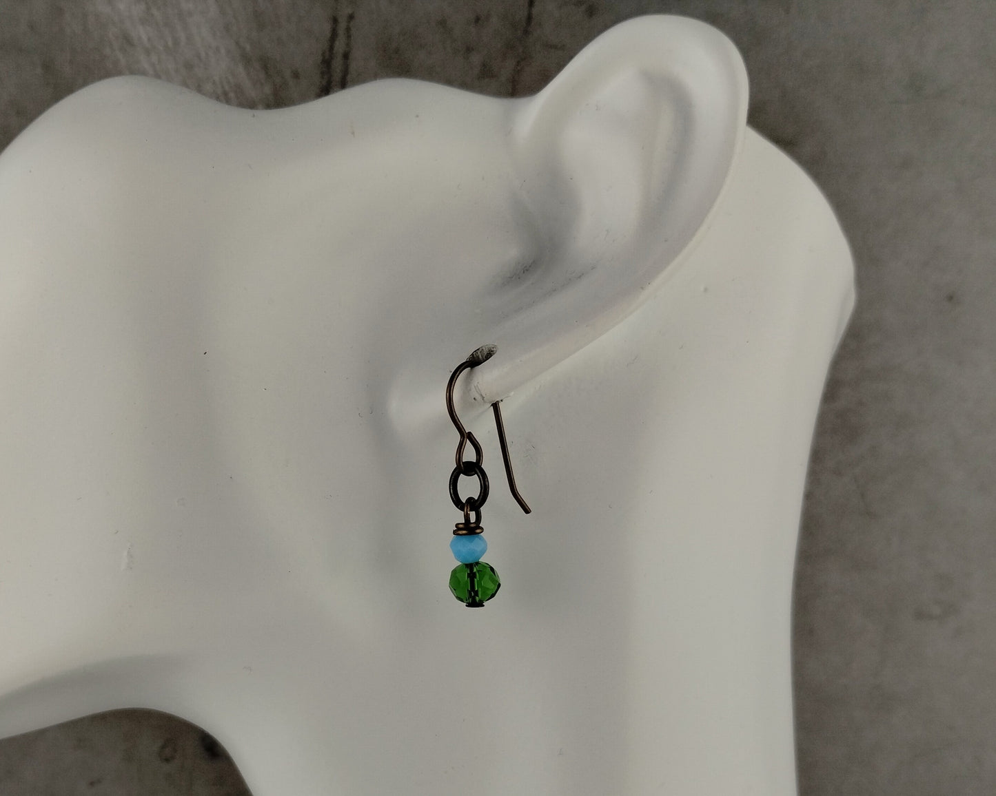 Earring with green and blue beads on a mannequin ear