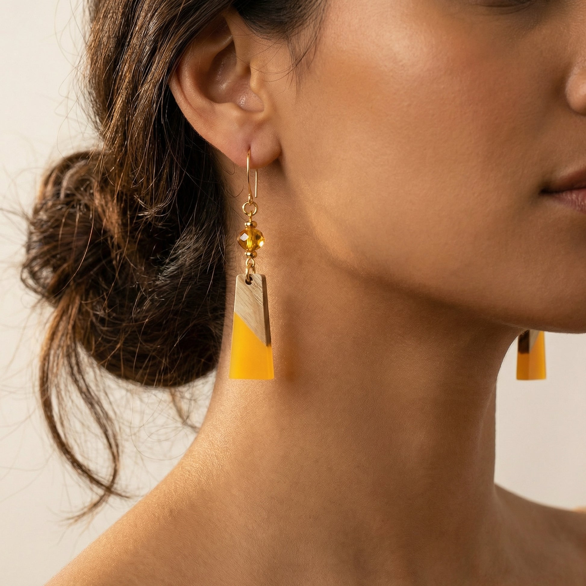 Close-up of a woman wearing gold earrings with yellow accents.