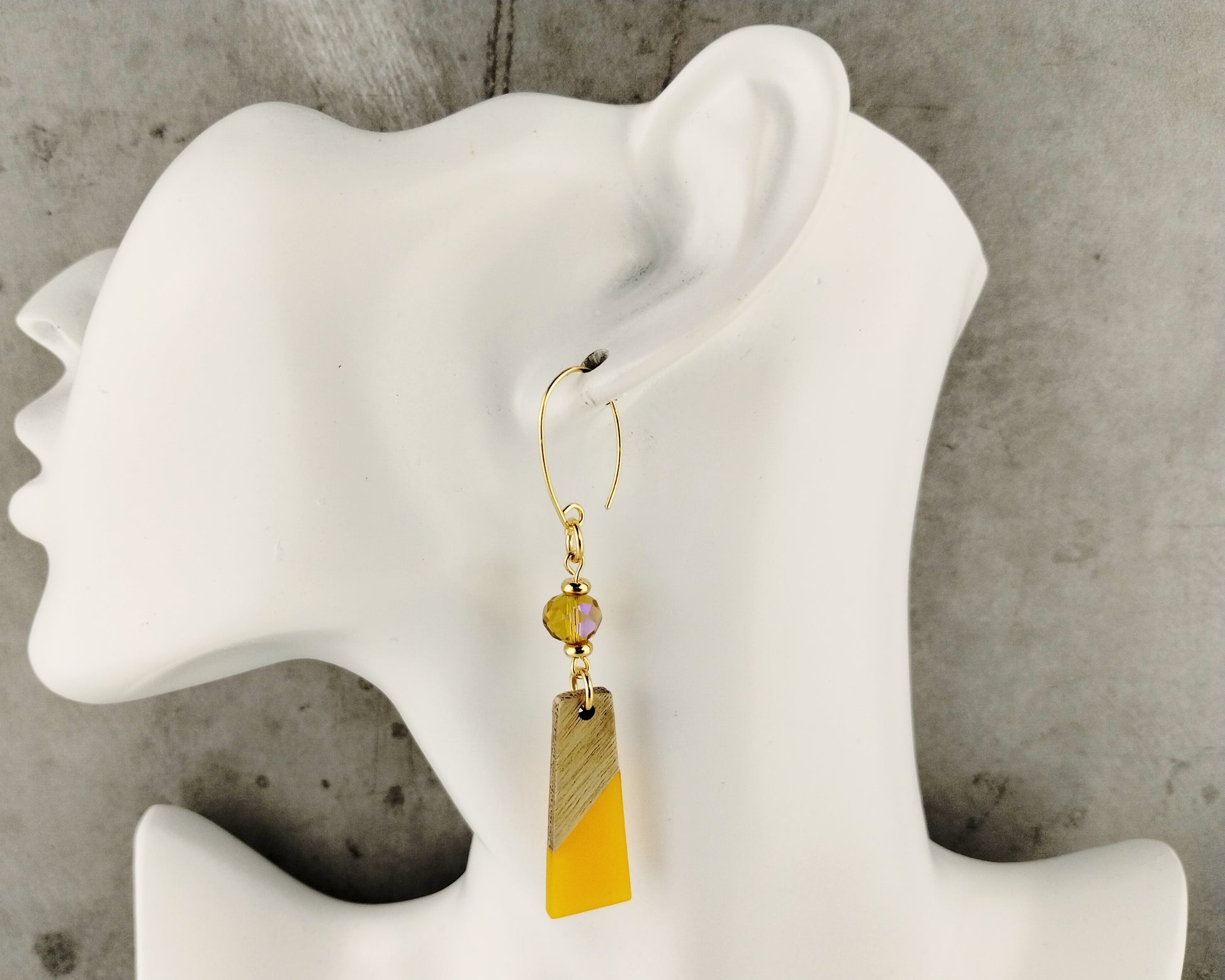 Earring with a yellow and brown pendant on a mannequin ear against a gray background