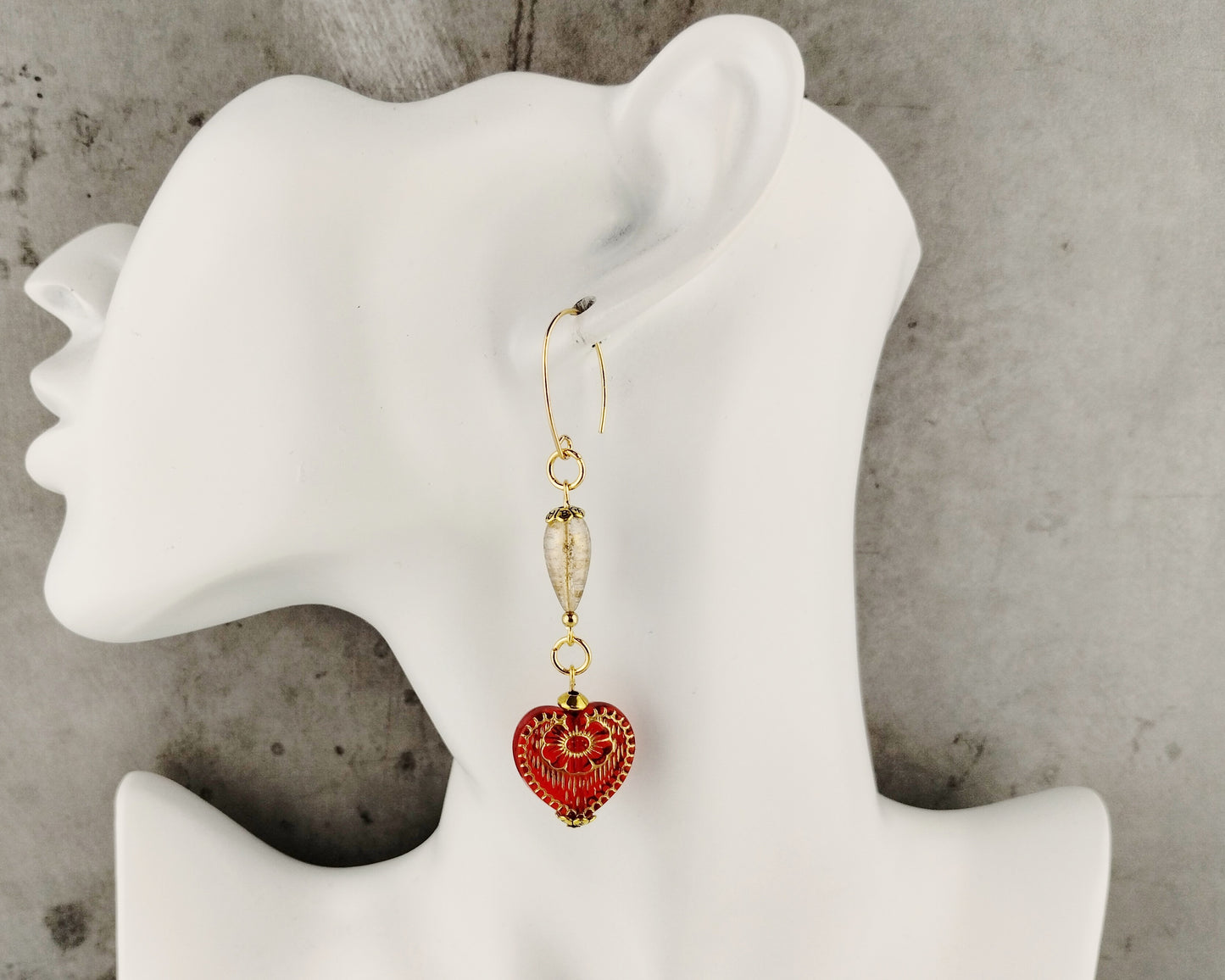 Red heart-shaped earrings on a white mannequin ear with a gray background