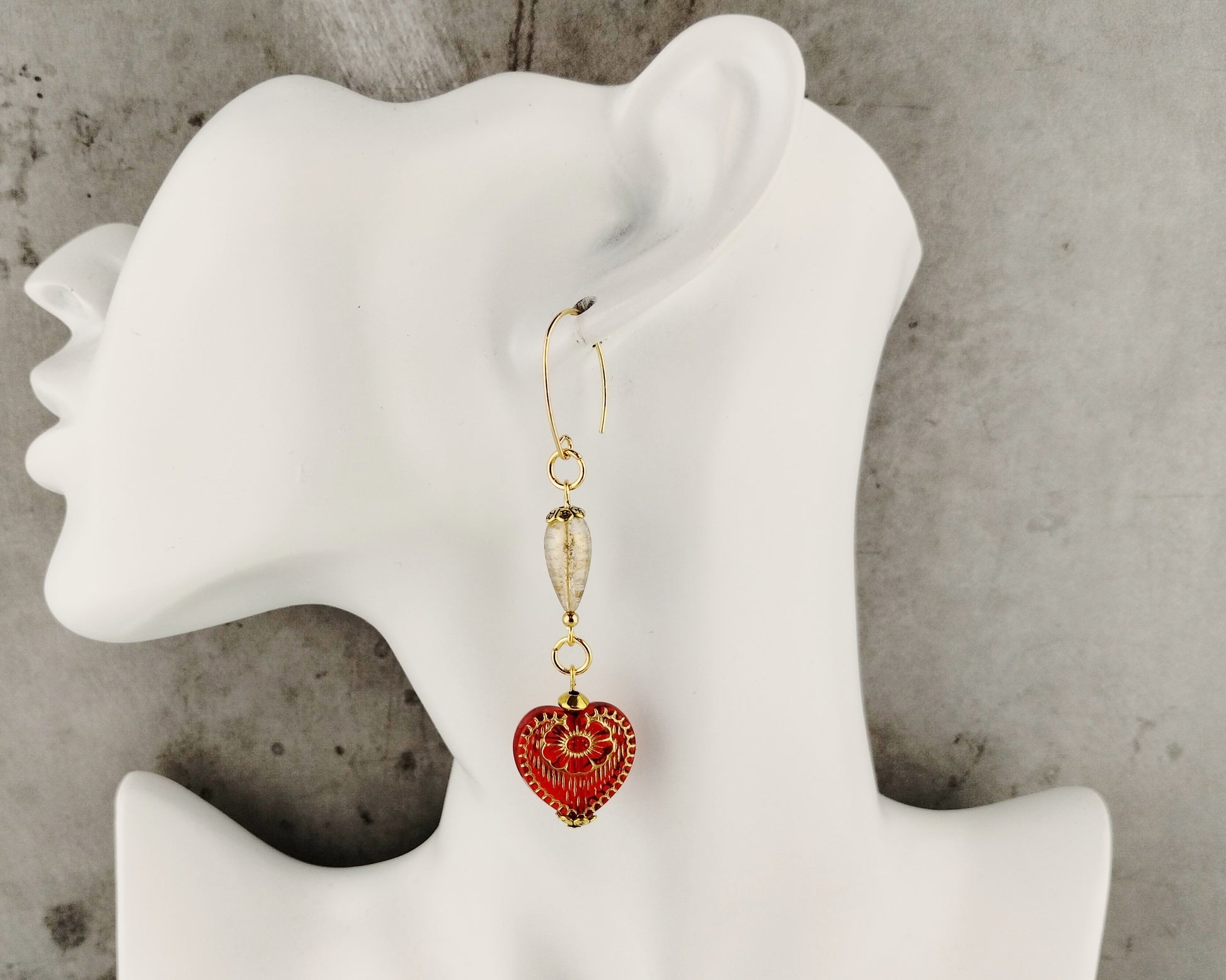 Red heart-shaped earrings on a white mannequin ear with a gray background