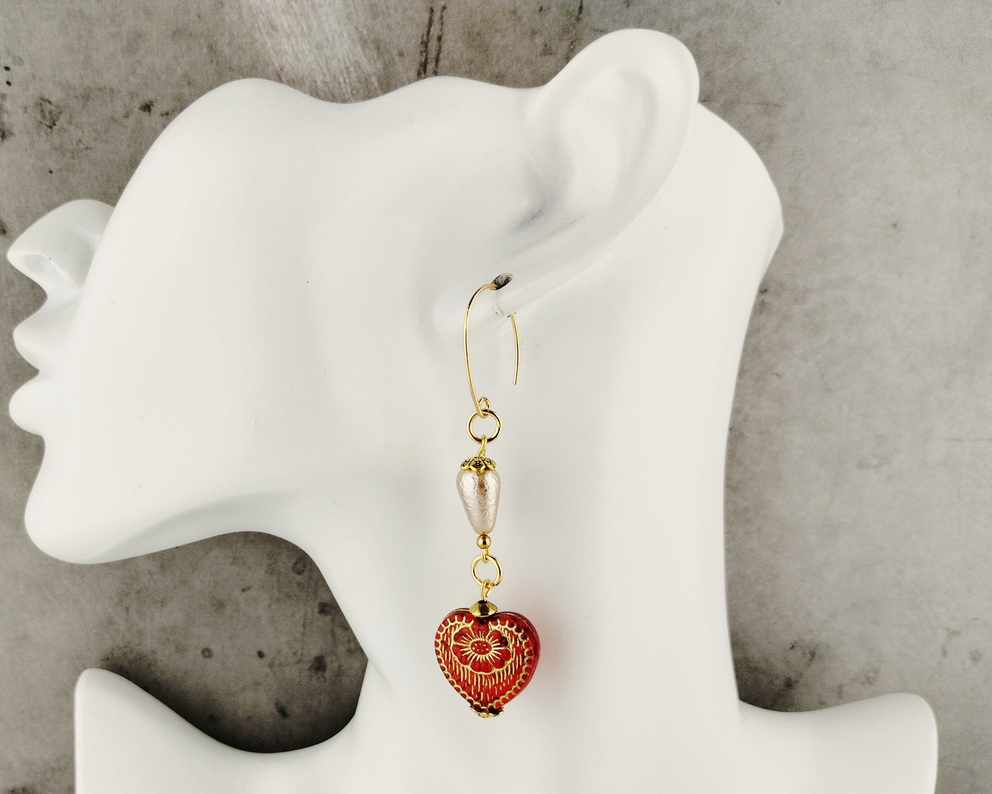 Earring with red heart-shaped pendant on a white mannequin bust against a gray background