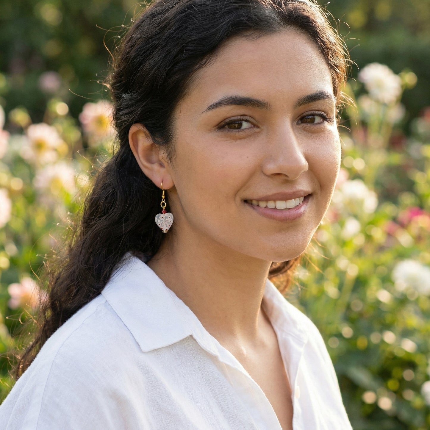 Woman with heart-shaped earrings standing in a garden.