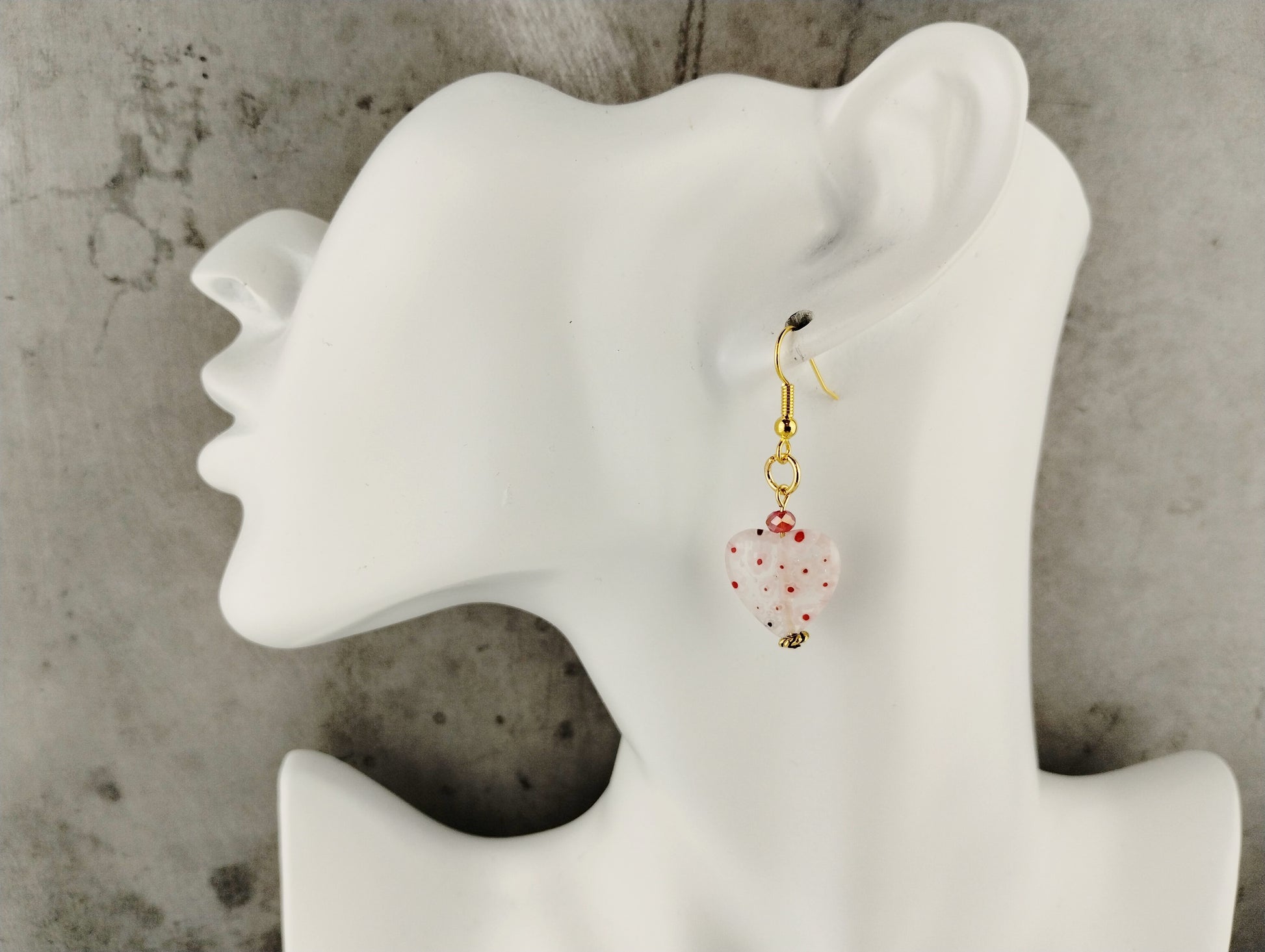 Earrings on a white mannequin ear with a concrete background