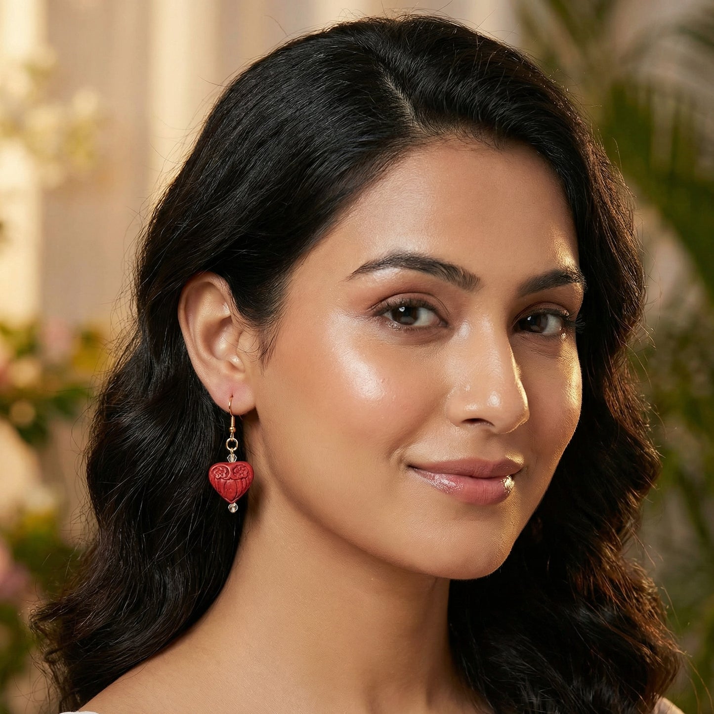 Woman wearing red heart-shaped earrings with a blurred floral background