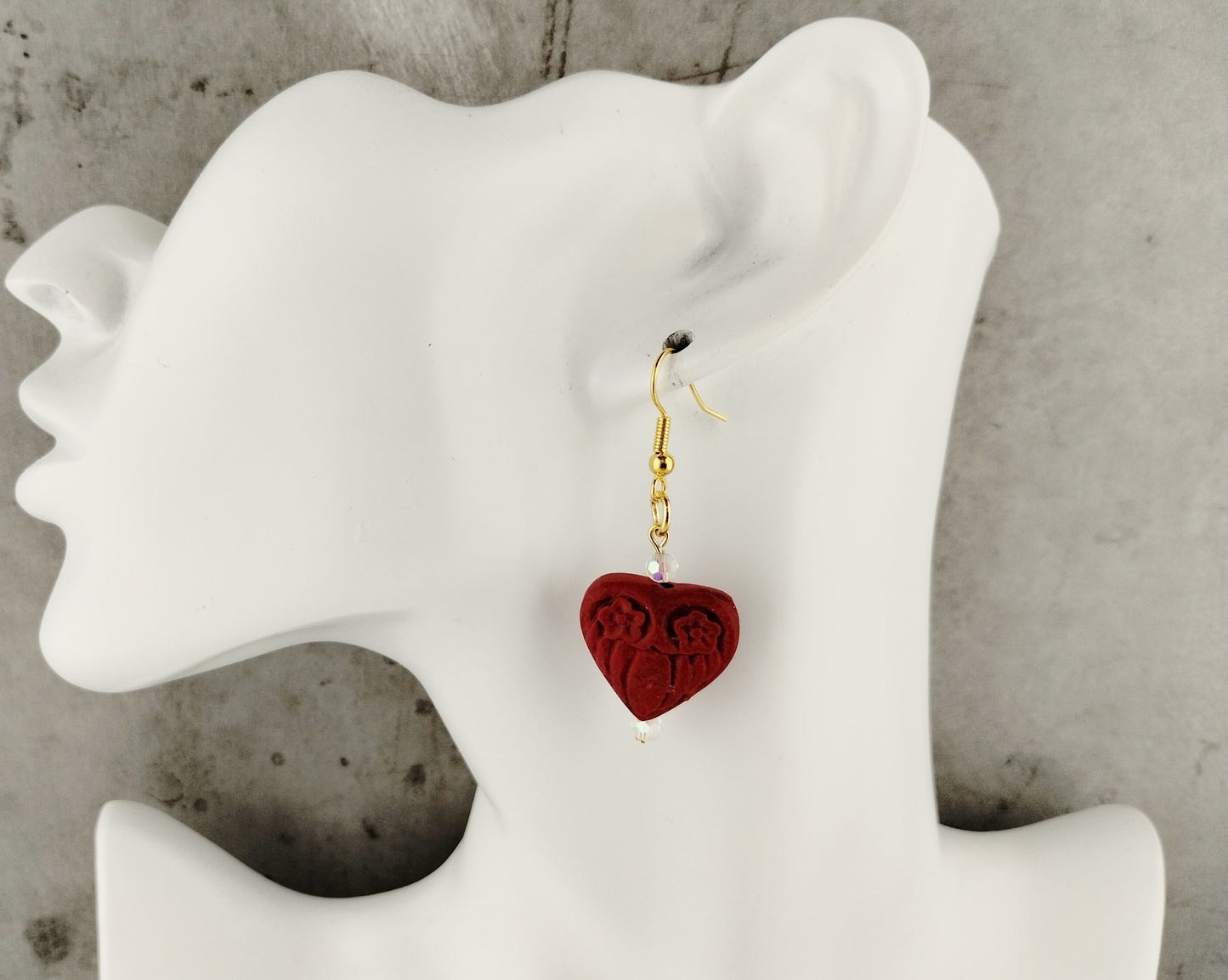 Red heart-shaped earring on a white mannequin ear with a gray background