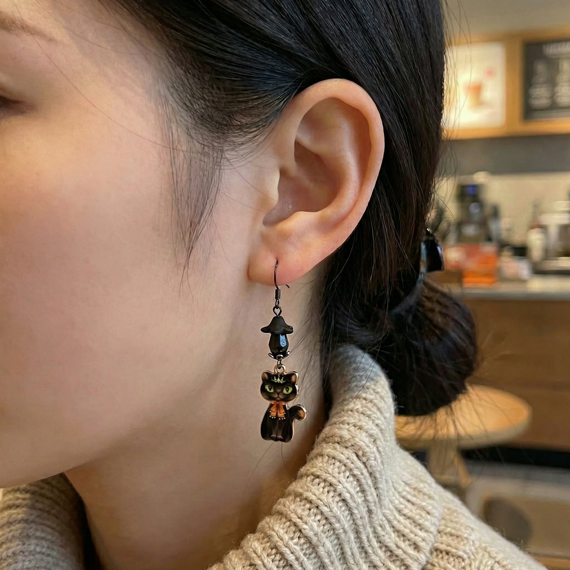 Close-up of a person wearing a black cat-shaped earring in a kitchen setting