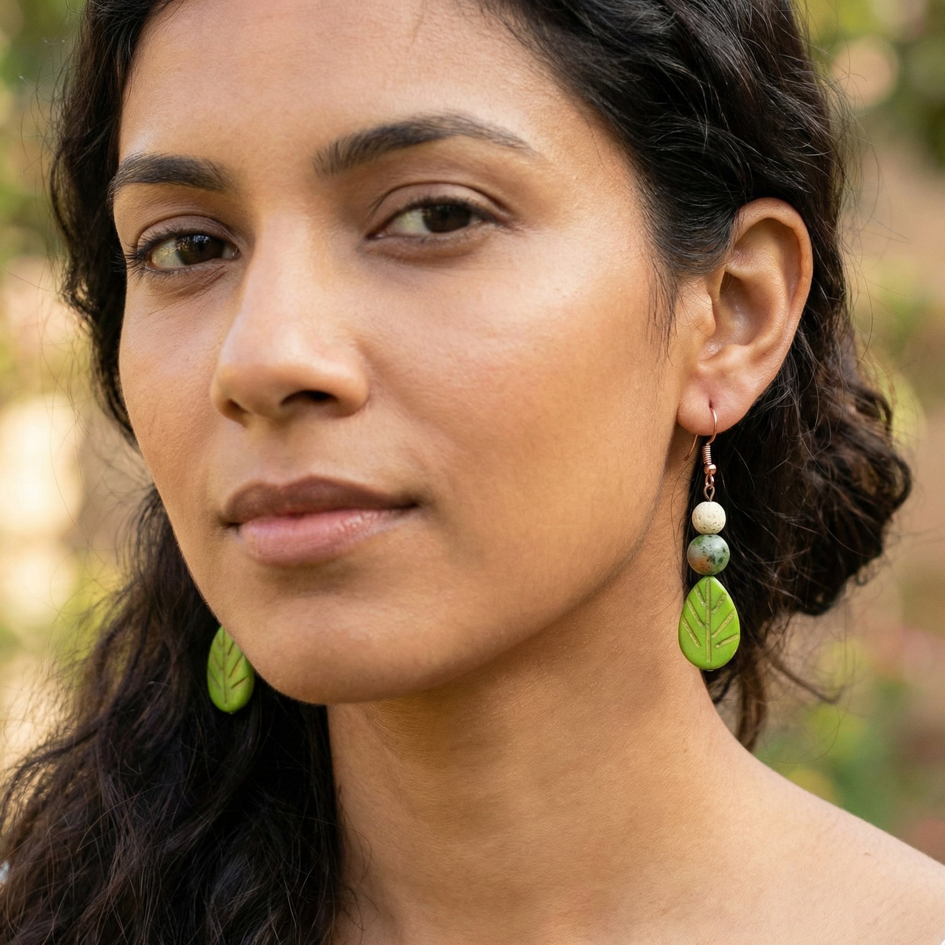 Woman wearing green leaf-shaped earrings outdoors