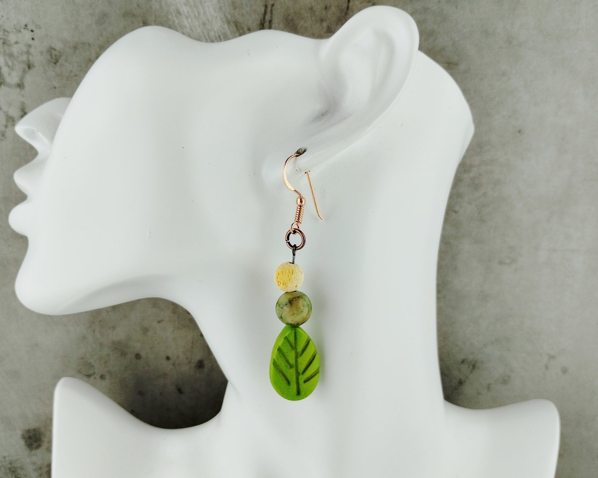 Green leaf-shaped earrings on a white mannequin ear with a concrete background