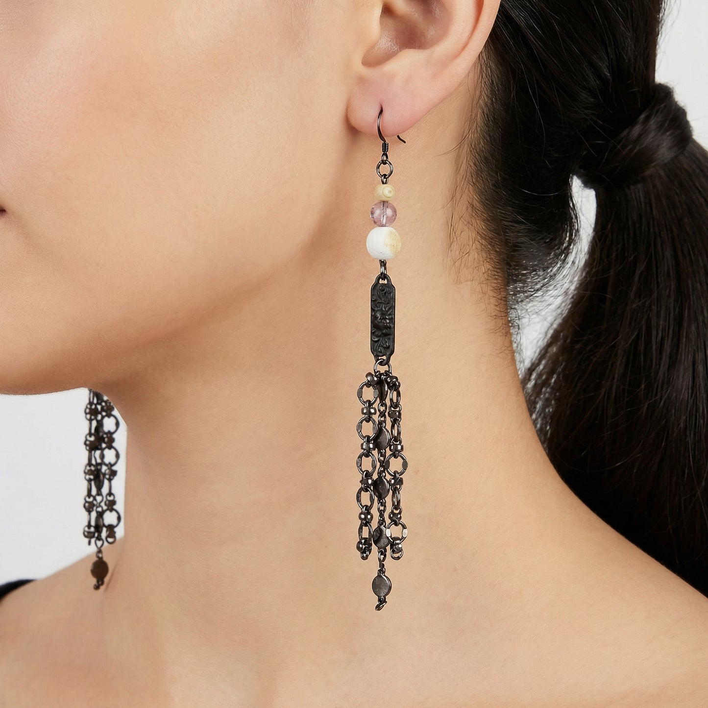 Close-up of a person wearing long, dangling earrings with beads.