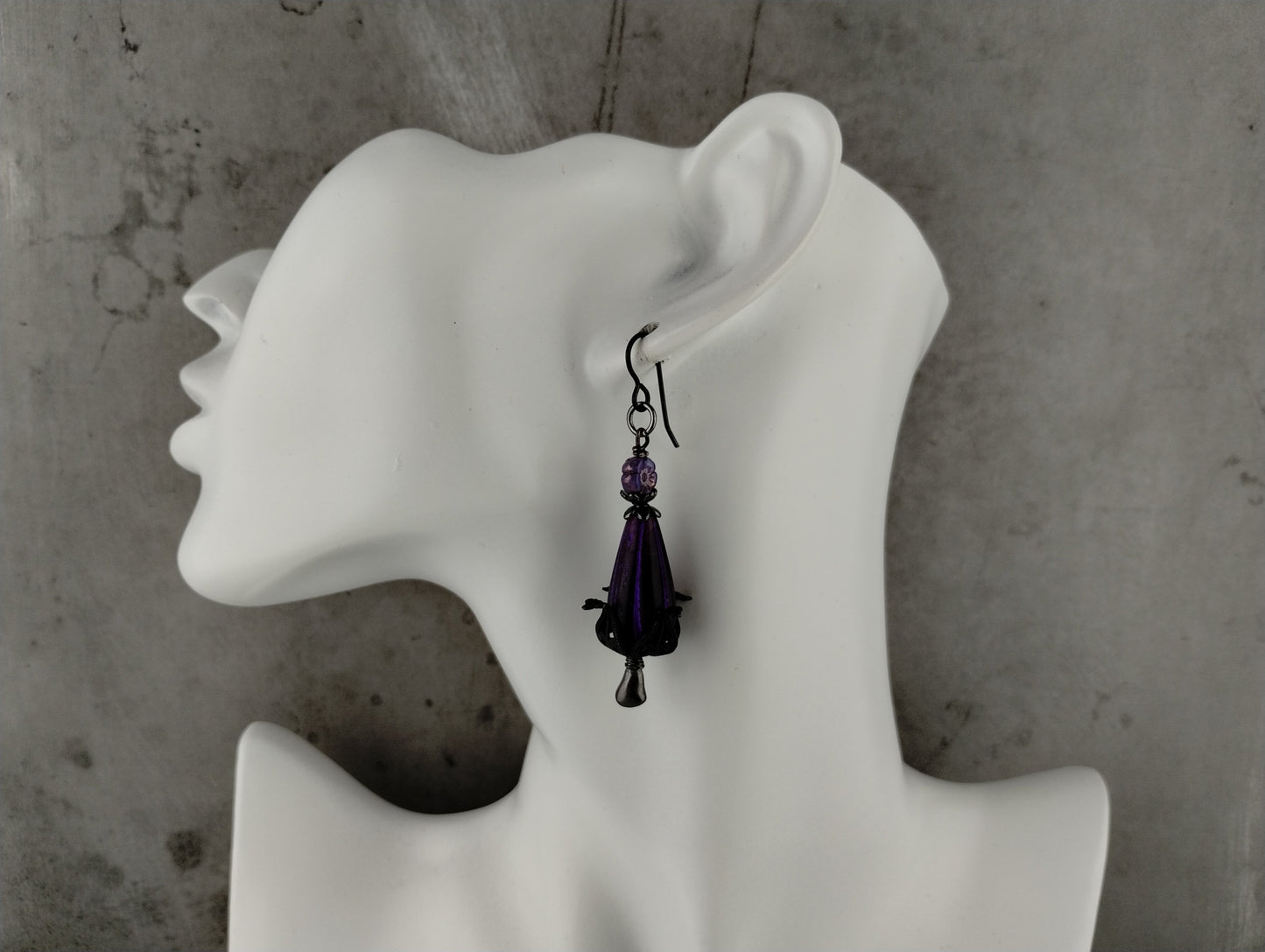 Purple teardrop earring on a white mannequin ear against a gray background