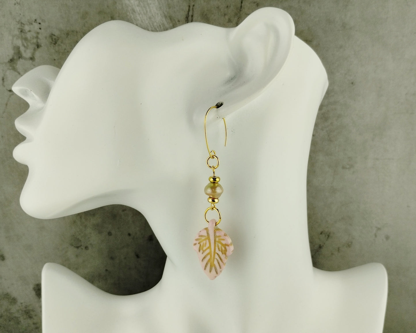 Gold earrings with pink floral design on a white mannequin ear against a gray background